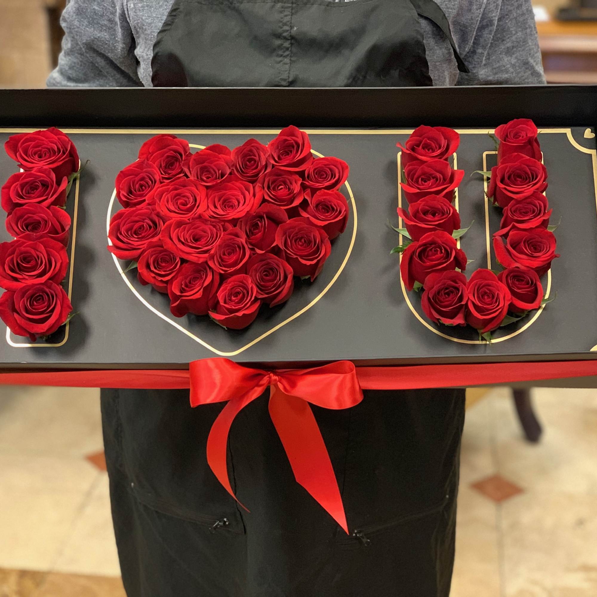 Red roses arranged to spell I love you in a black gift box