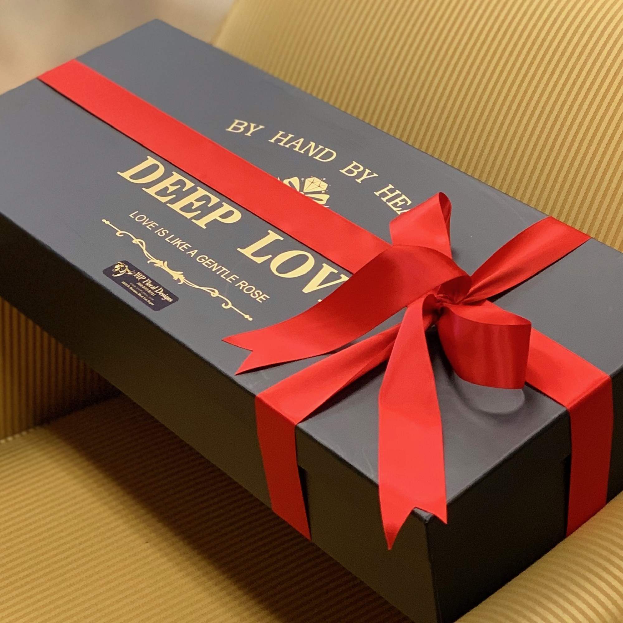 Black gift box with a red ribbon and gold lettering