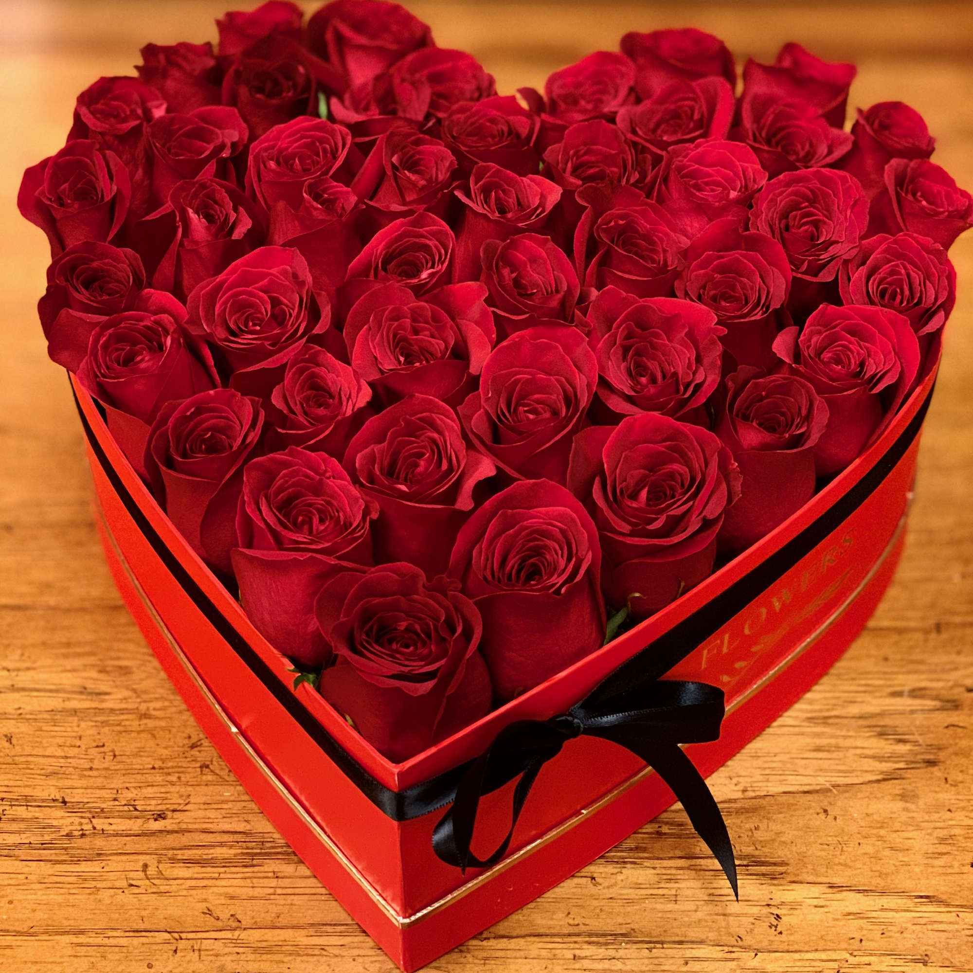 Heart-shaped box filled with red roses and tied with a black ribbon
