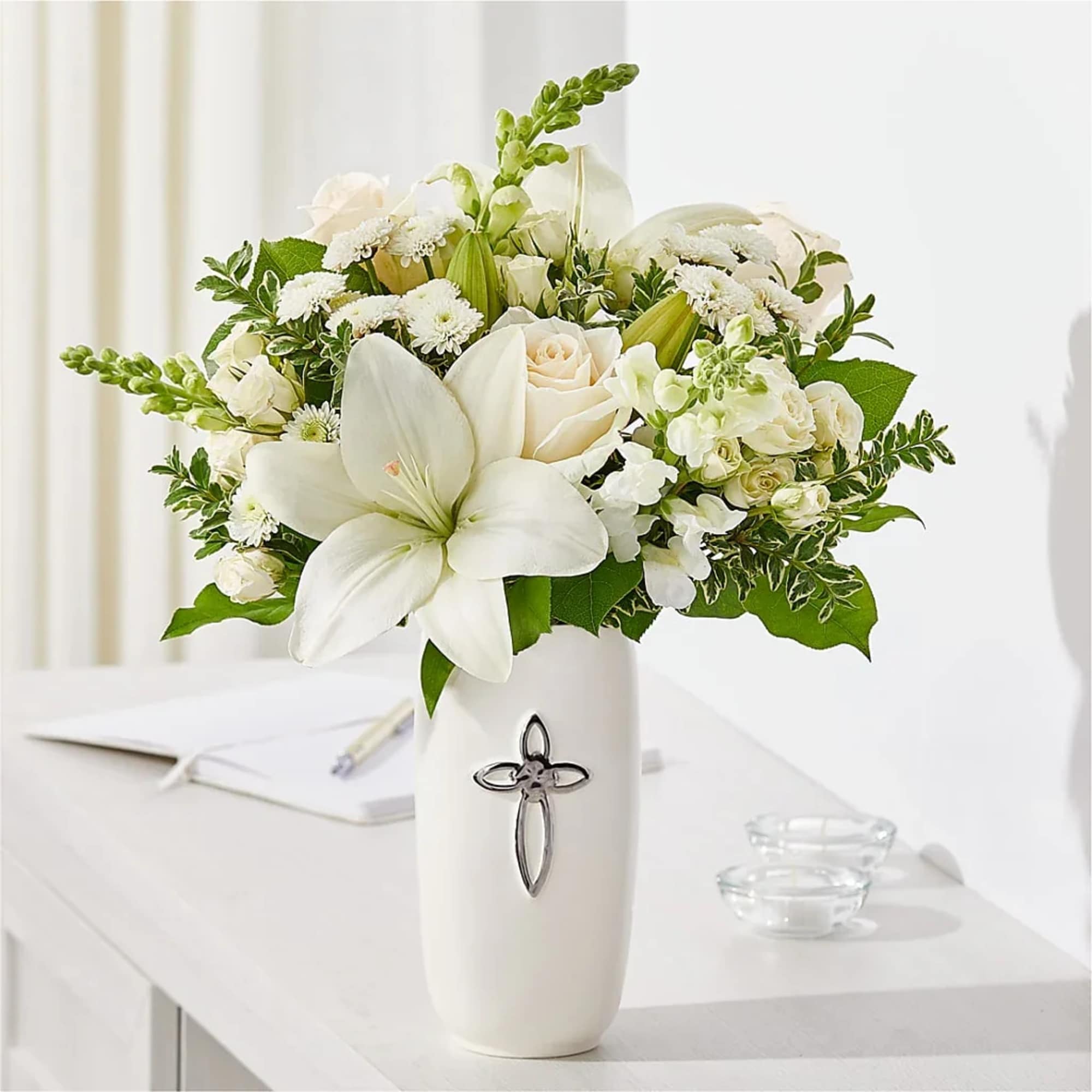 White floral arrangement in a tall vase with a cross emblem