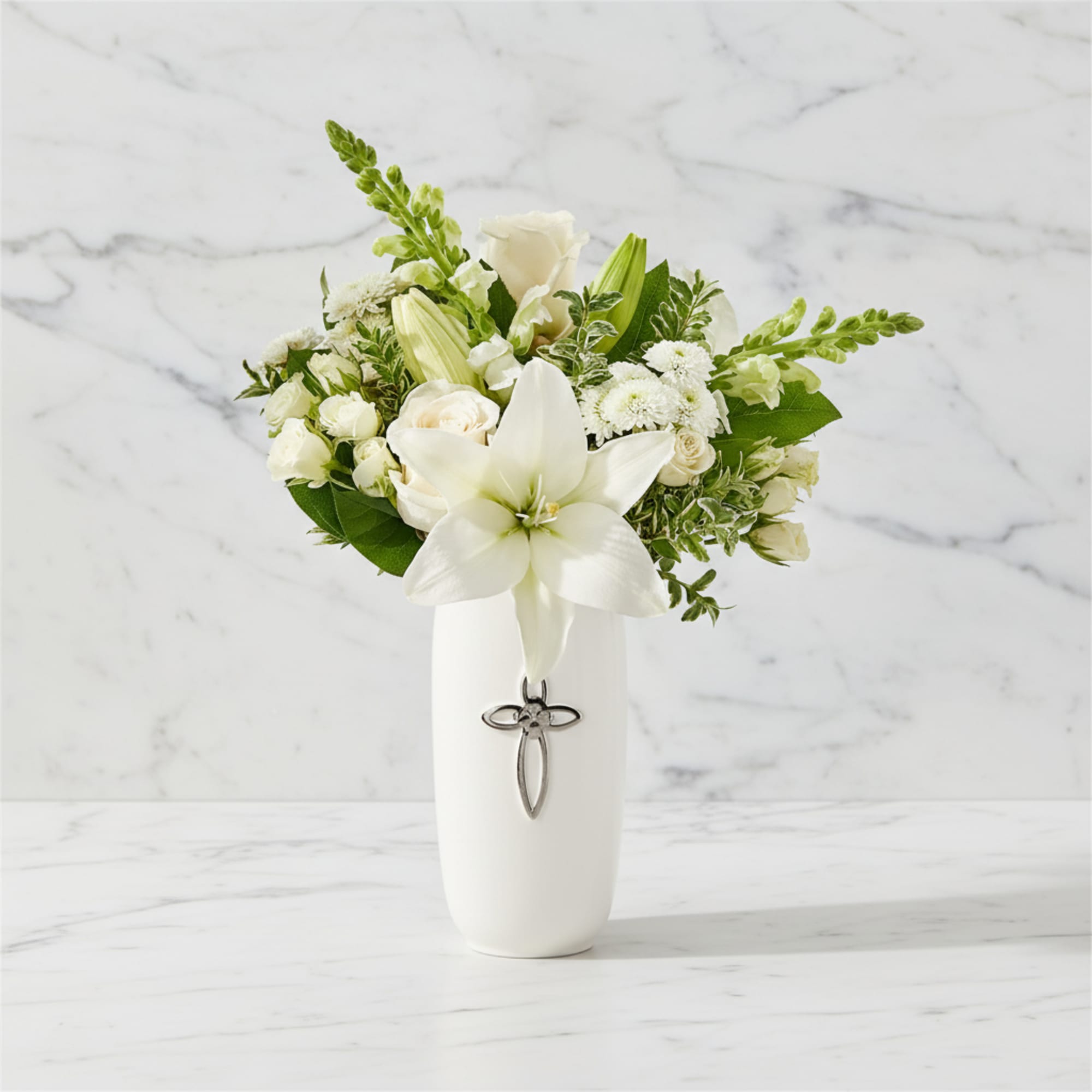 White lily and rose arrangement in a white vase with a cross charm