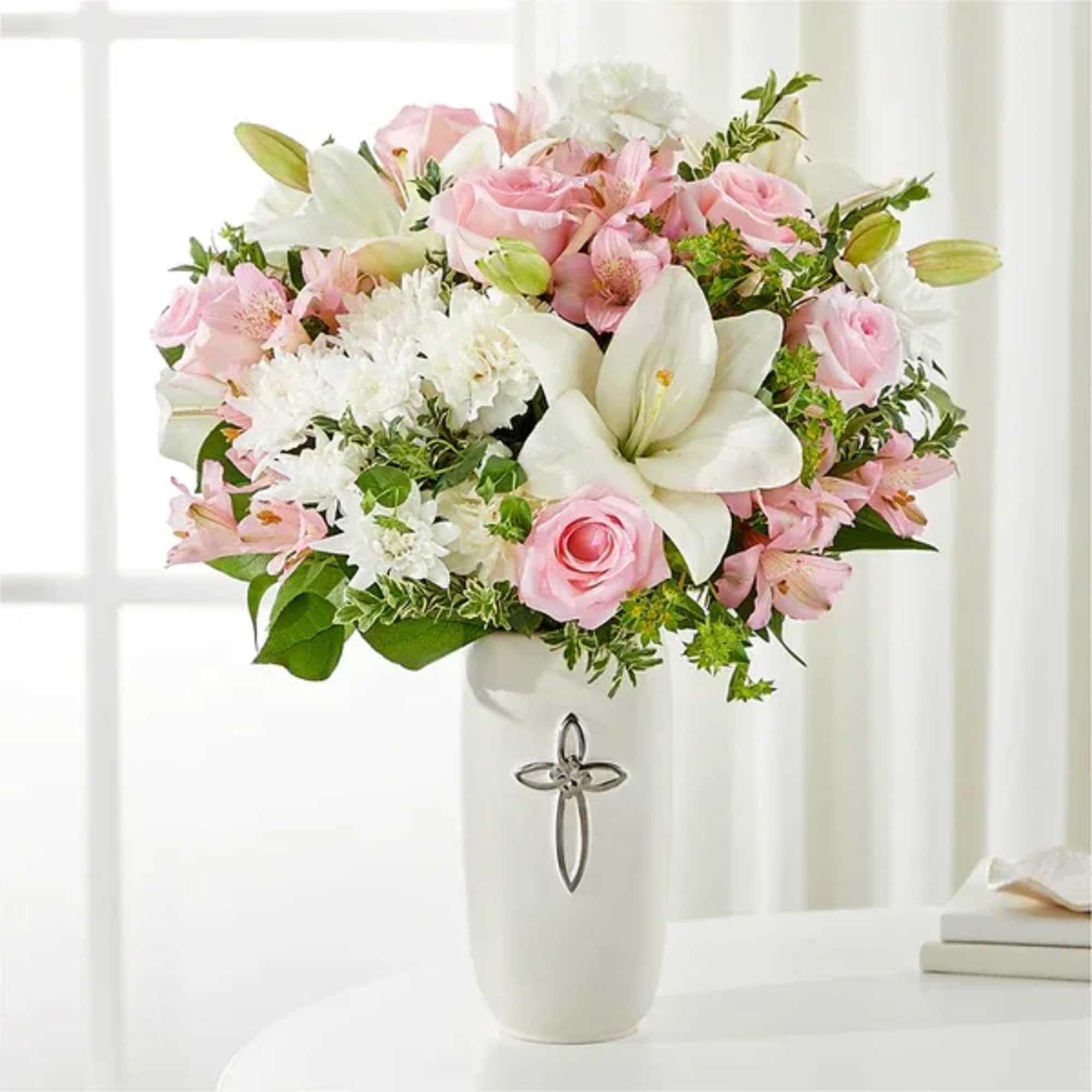 Pink and white flower arrangement in a white vase with a cross emblem