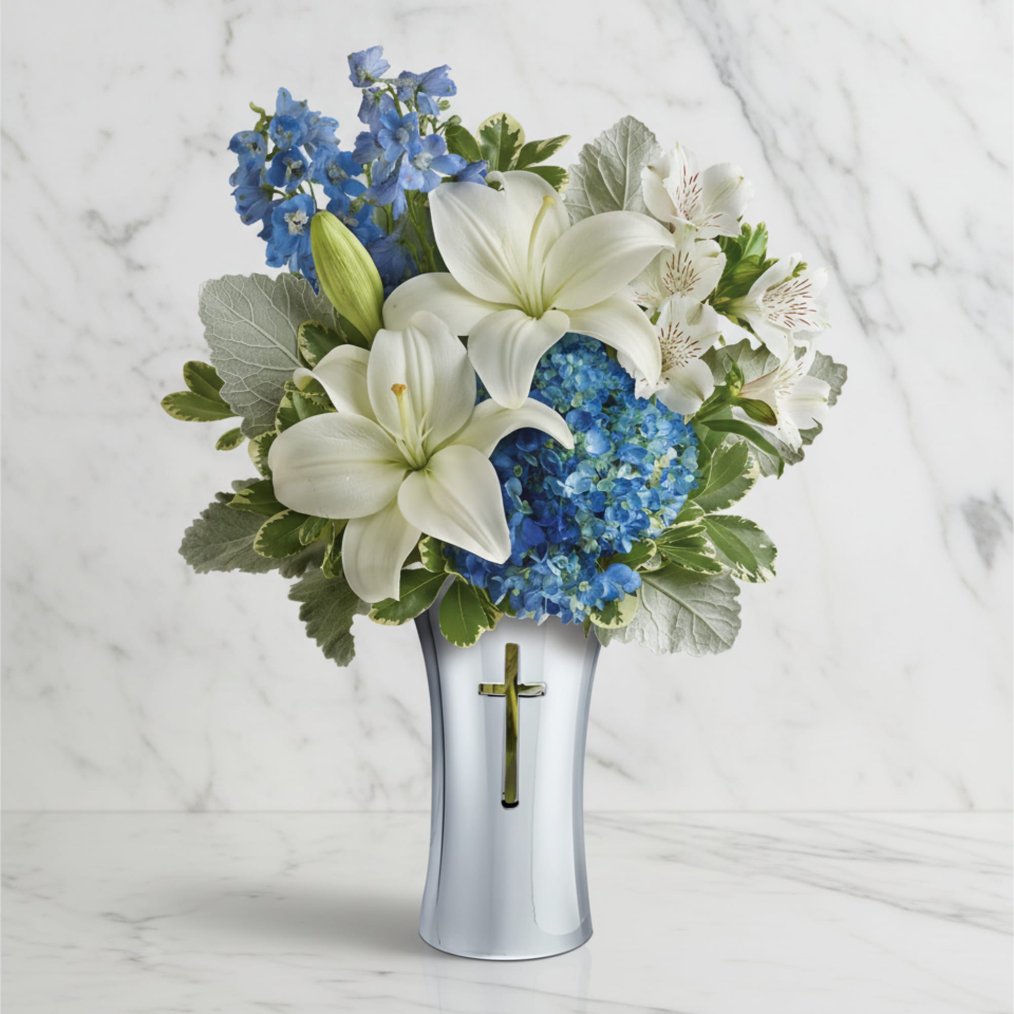 White lilies and blue flowers in a silver vase with a cross