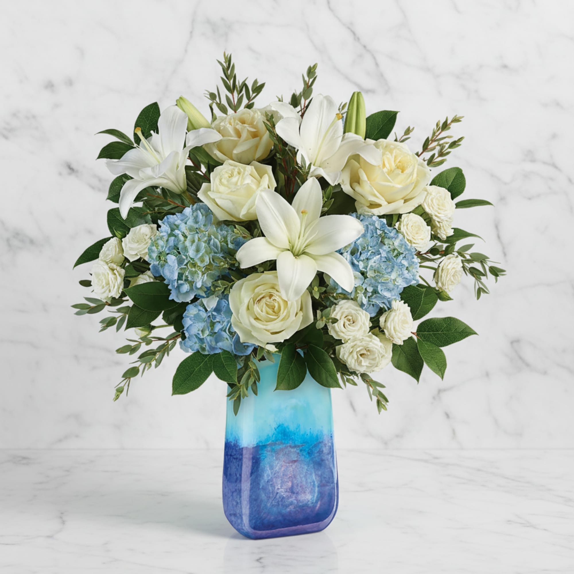 White lilies and roses with blue hydrangeas in a blue glass vase