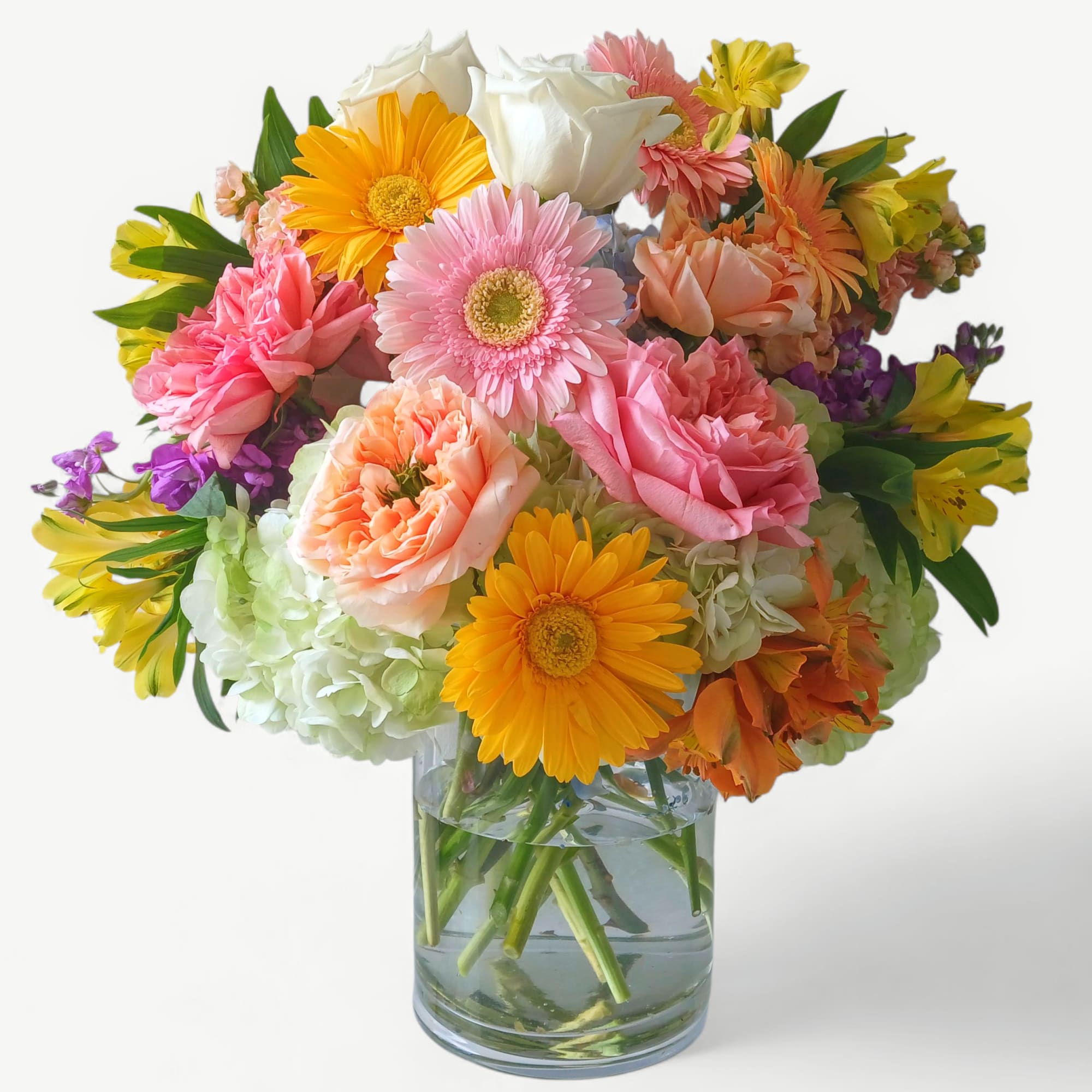 Bright mixed bouquet of yellow gerbera daisies, pink roses, and other blooms in a clear glass vase
