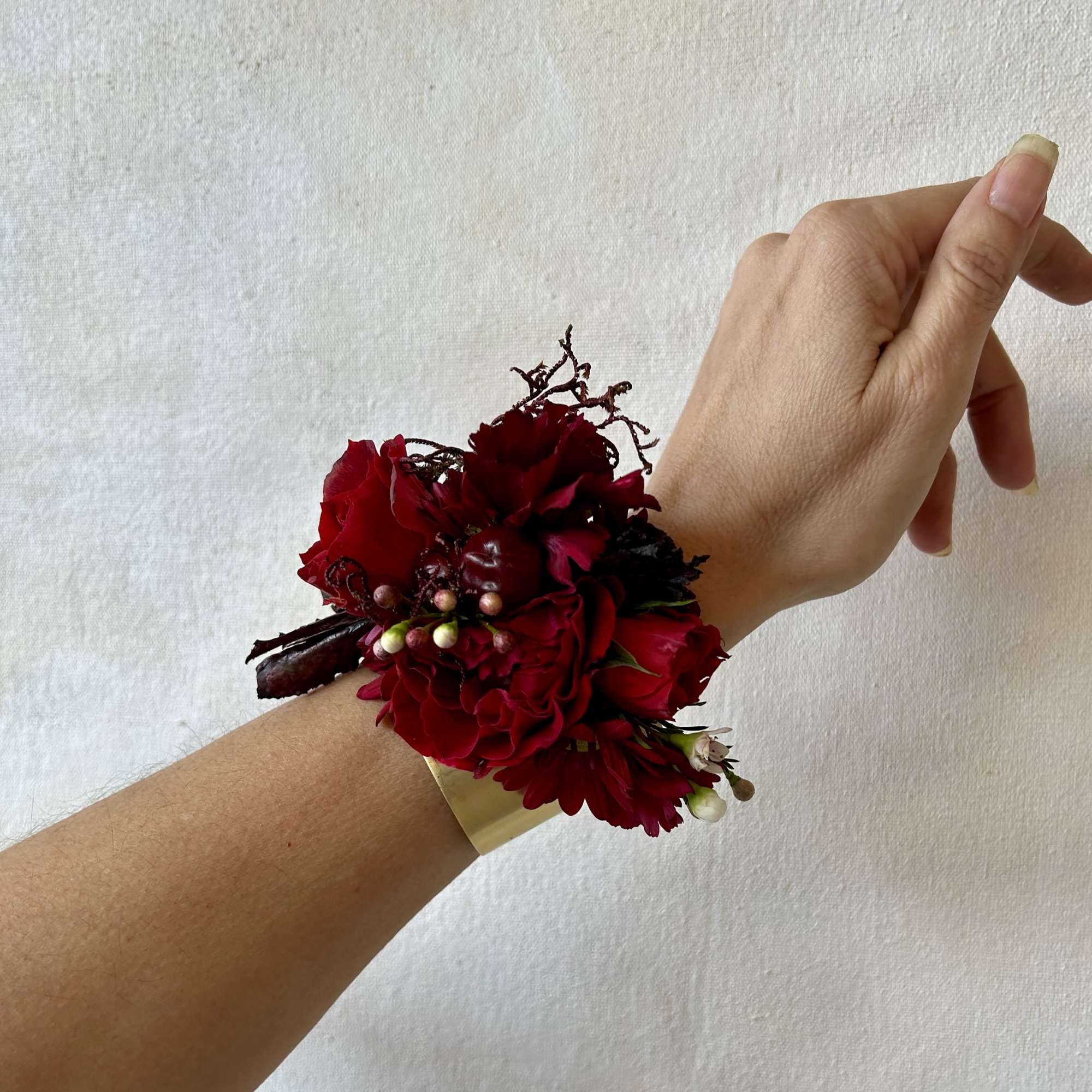 Red floral wrist corsage with a gold cuff bracelet