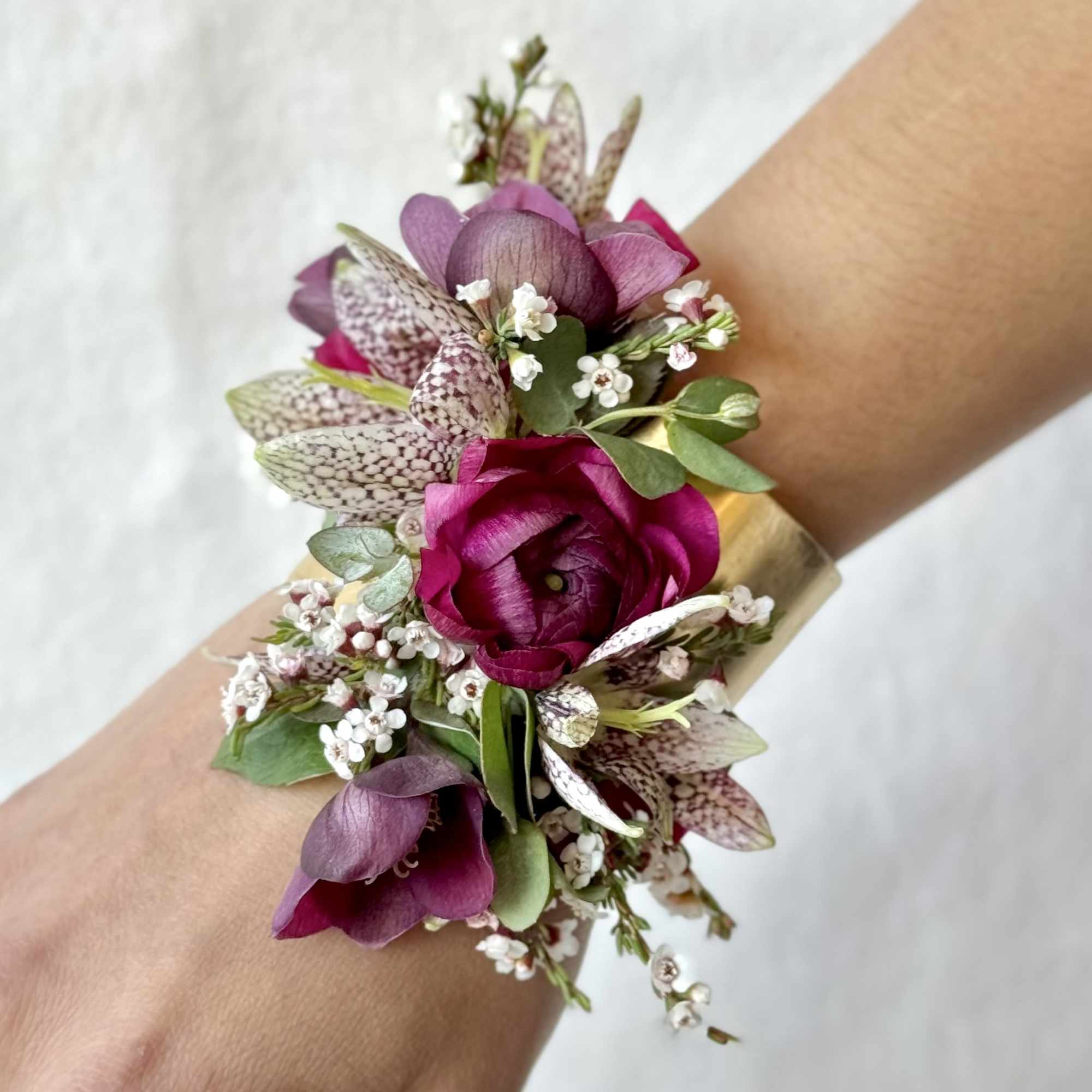 Purple floral wrist corsage with small white blossoms and green leaves