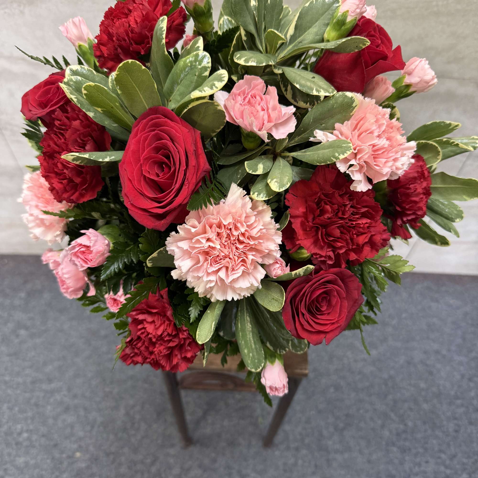 Round bouquet of red roses and pink carnations with variegated foliage in a compact arrangement