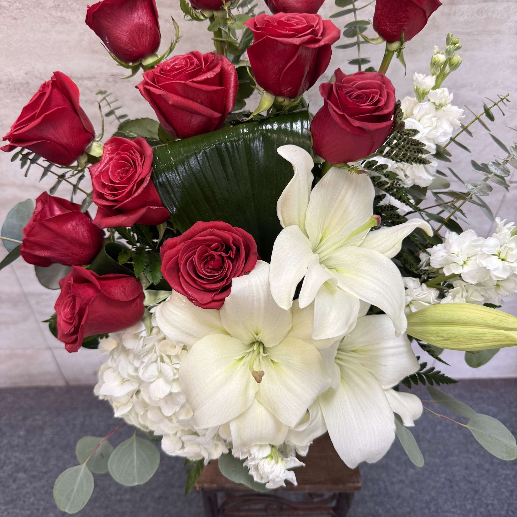 Tall arrangement of red roses with large white lilies and white hydrangea on a wooden stand