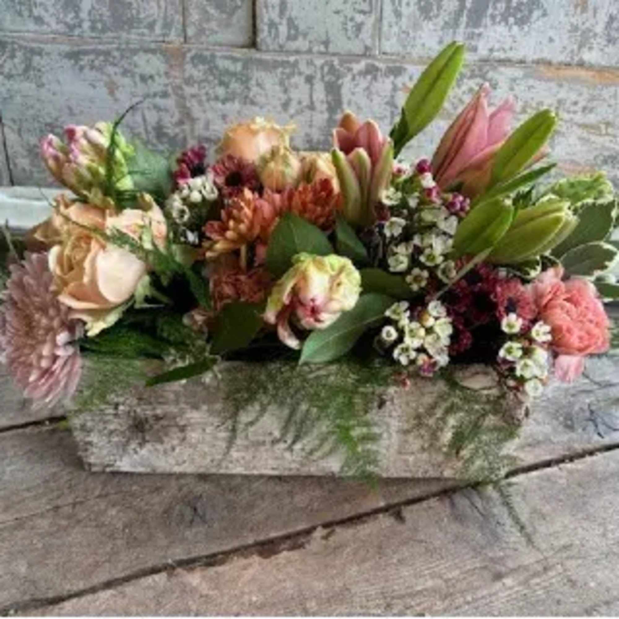 This stunning centerpiece features seasonal blooms in soft peaches and pinks, presented