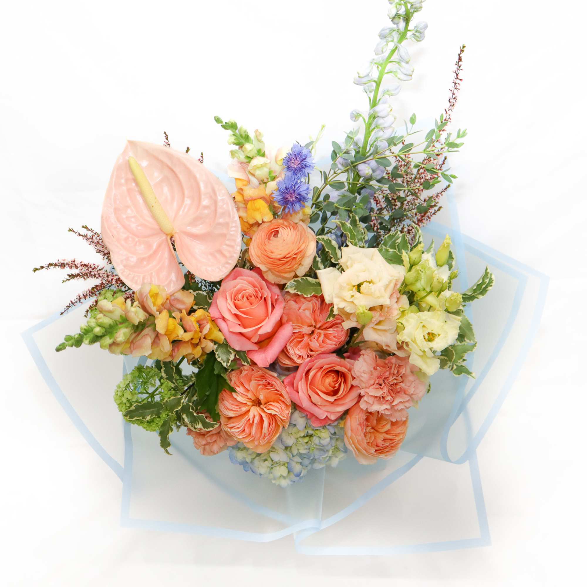 Pastel bouquet with roses, anthurium, and mixed blooms wrapped in blue paper
