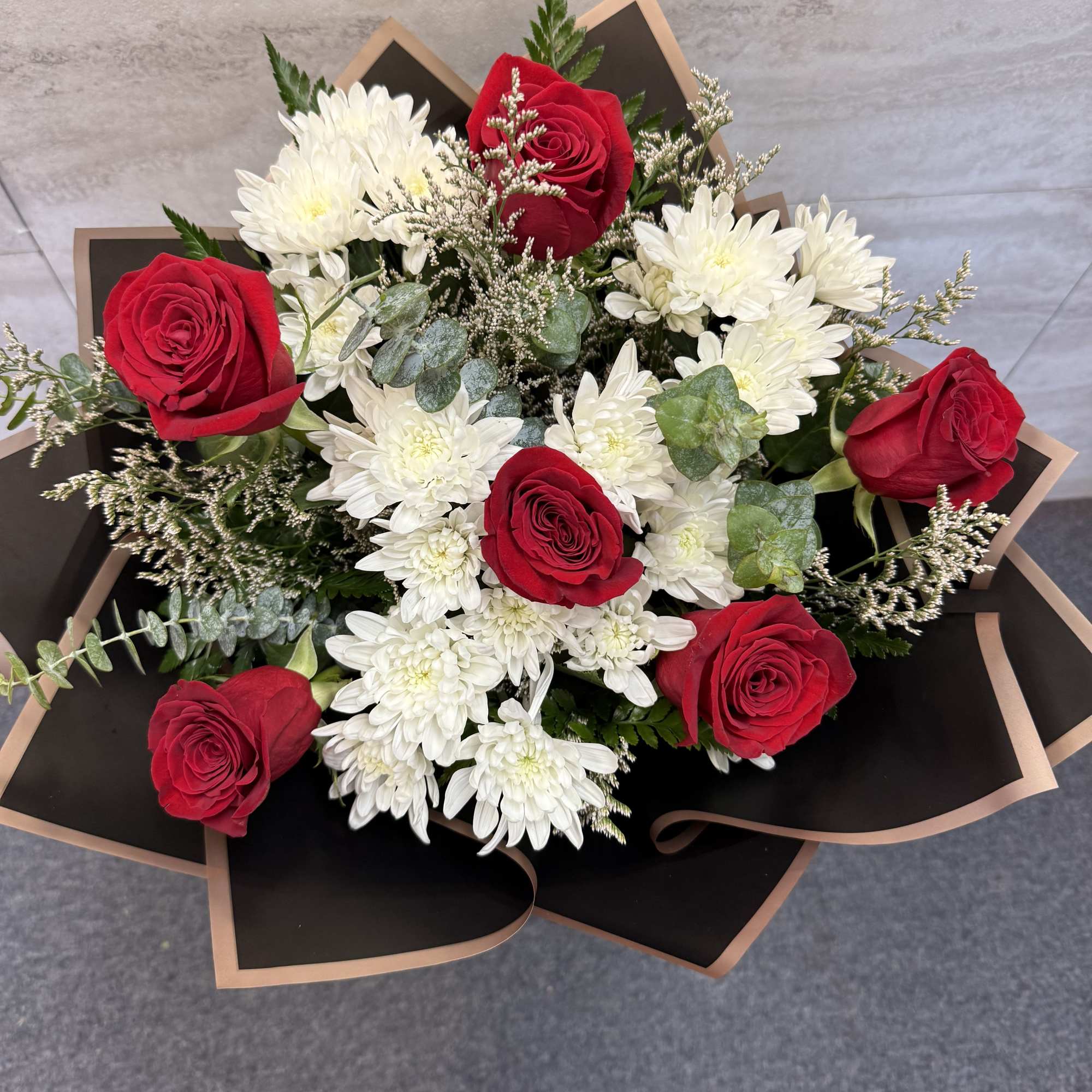 Bouquet of red roses and white chrysanthemums wrapped in black paper