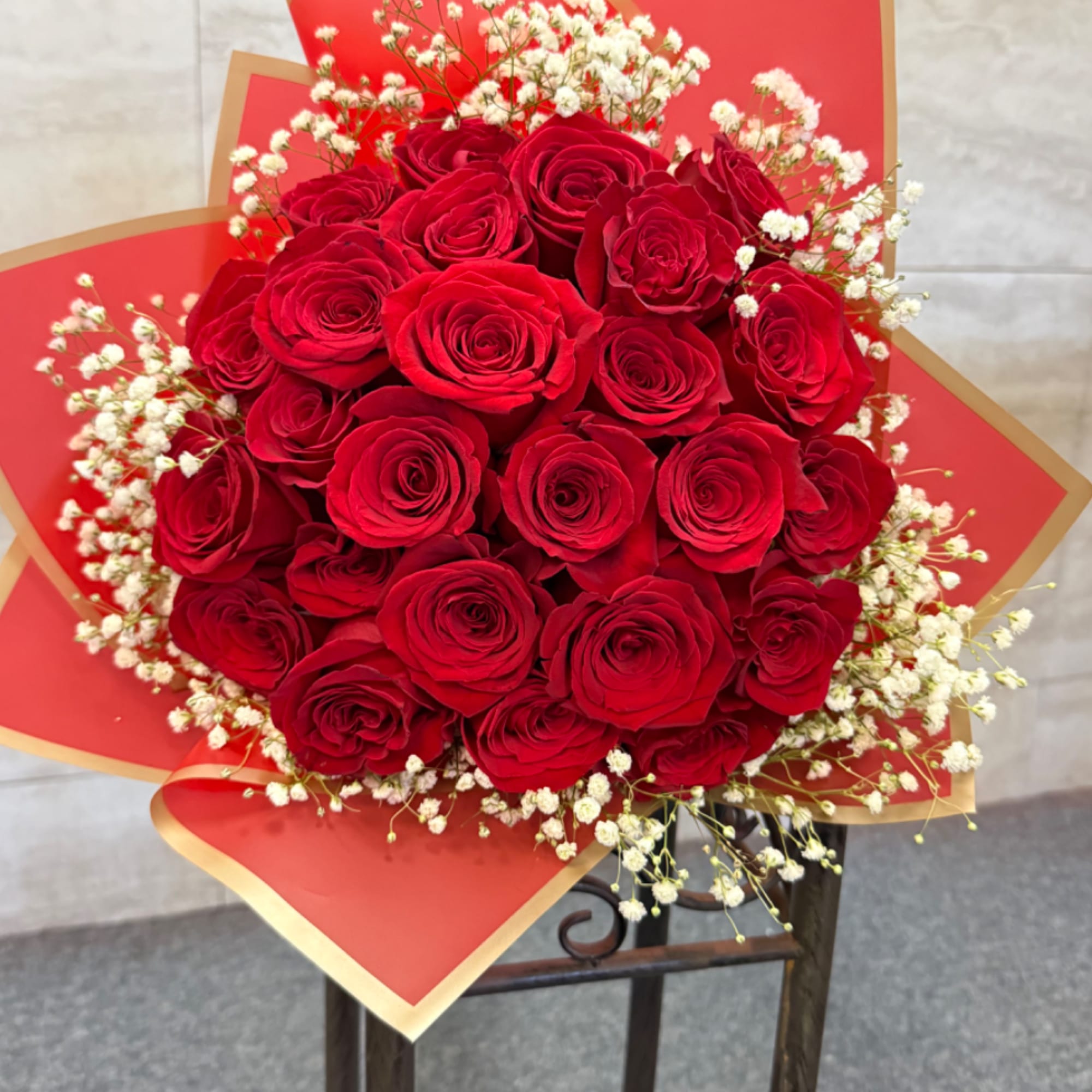 Round bouquet of red roses with white filler flowers wrapped in red and gold paper.