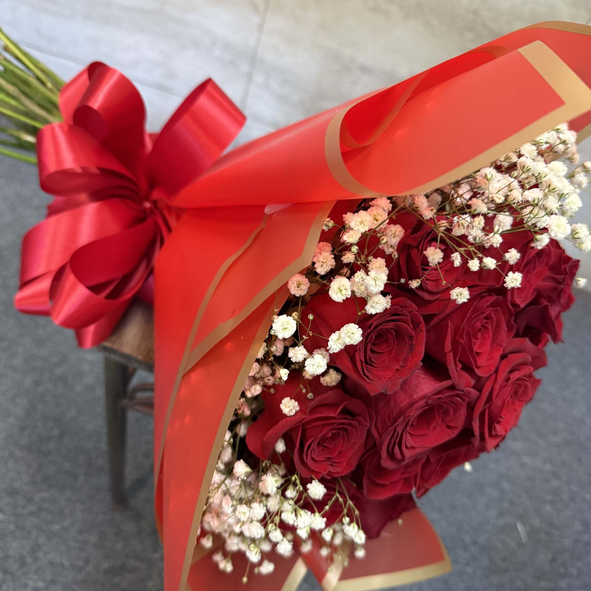 Hand-tied bouquet of red roses with white filler flowers wrapped in red paper and ribbon