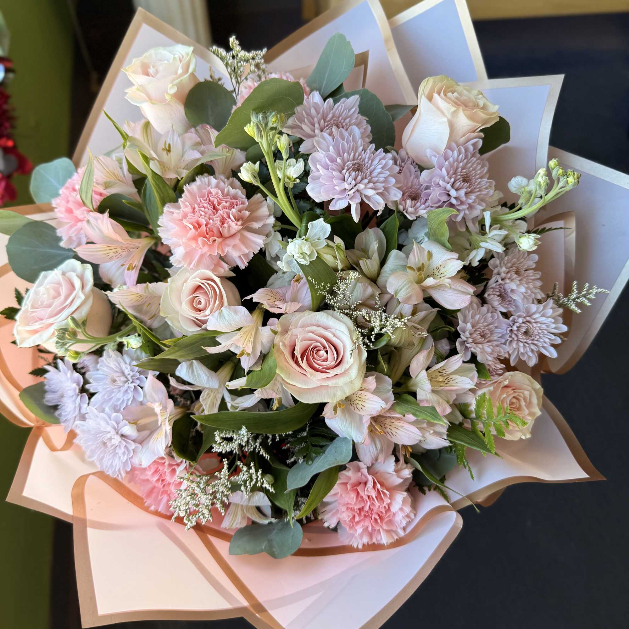 Bouquet of pale pink roses, carnations, and lavender mums wrapped in blush paper