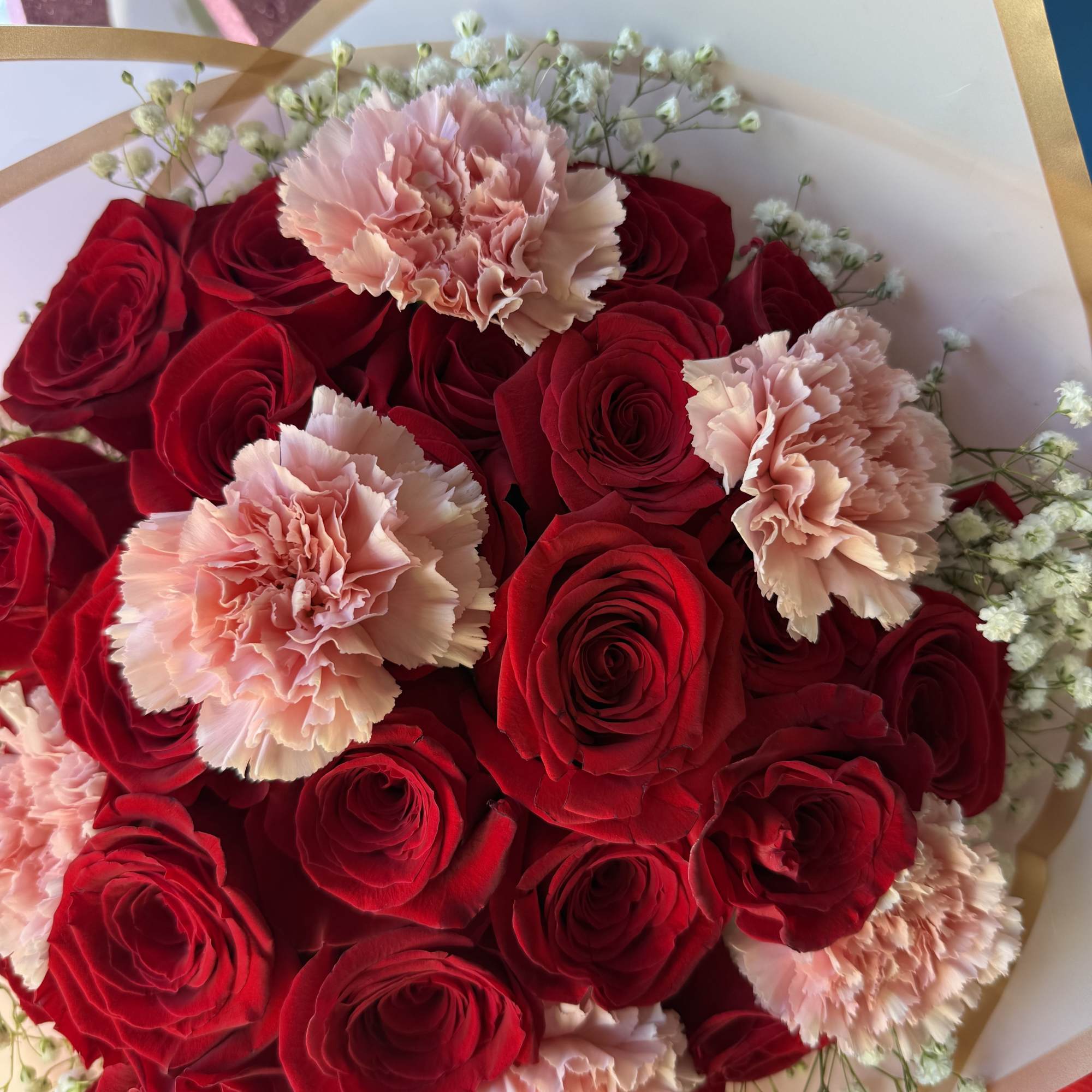 Bouquet of red roses and pale pink carnations wrapped in white paper
