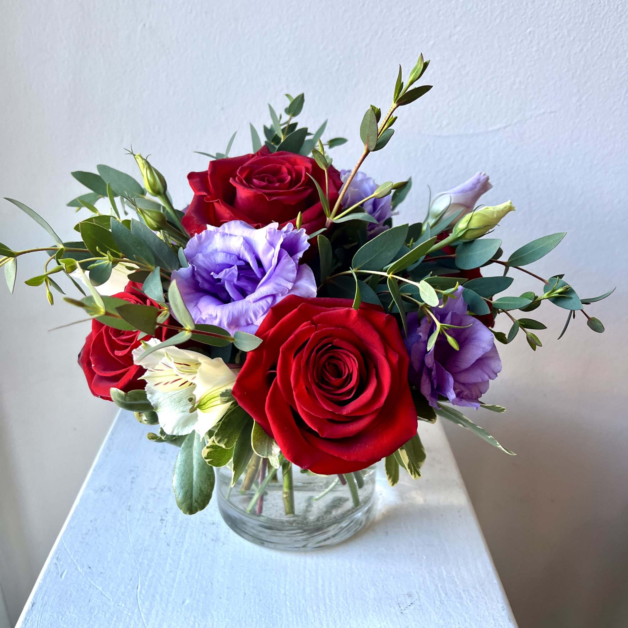 Red roses and purple blooms arranged in a clear glass vase