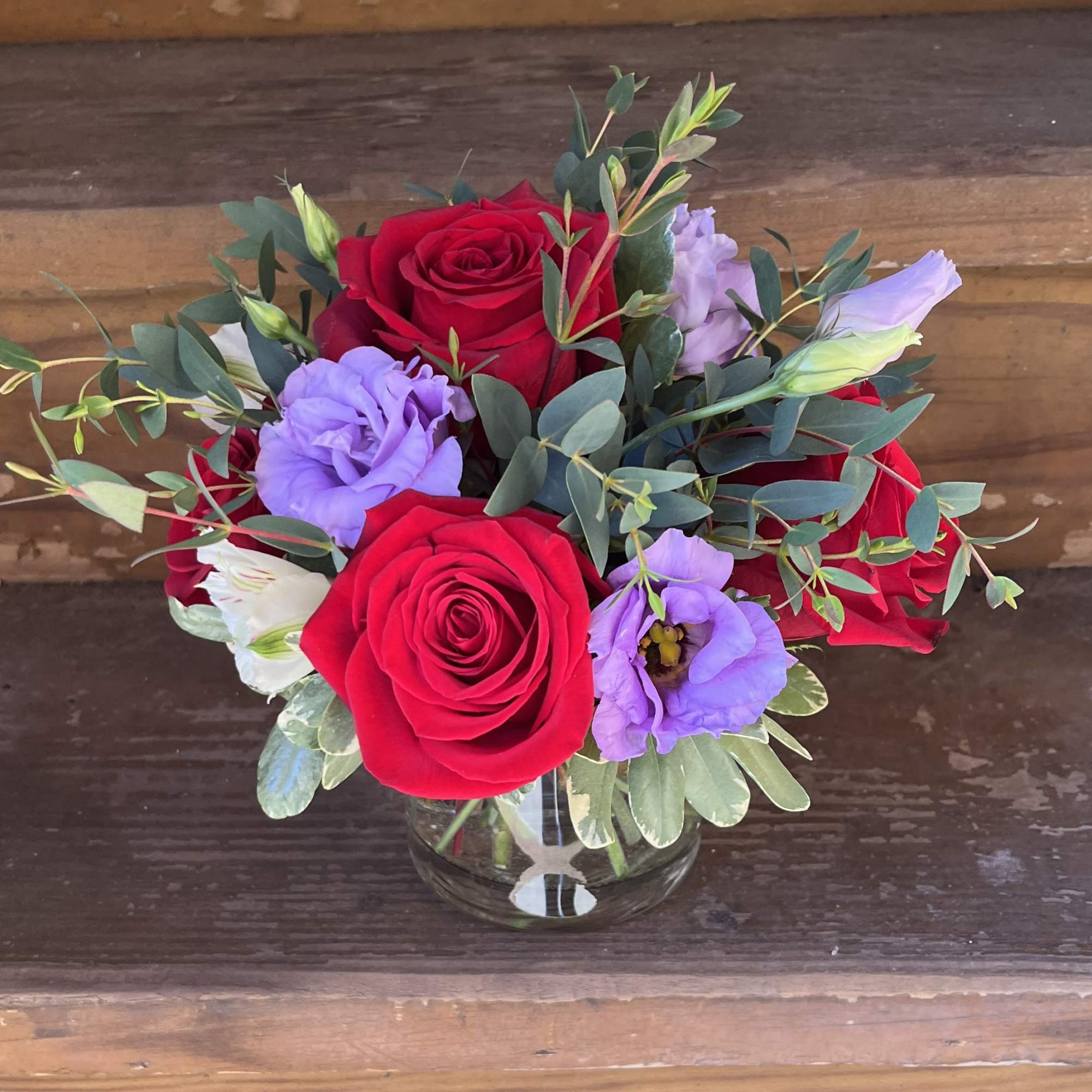 Red roses and lavender blooms in a clear glass vase