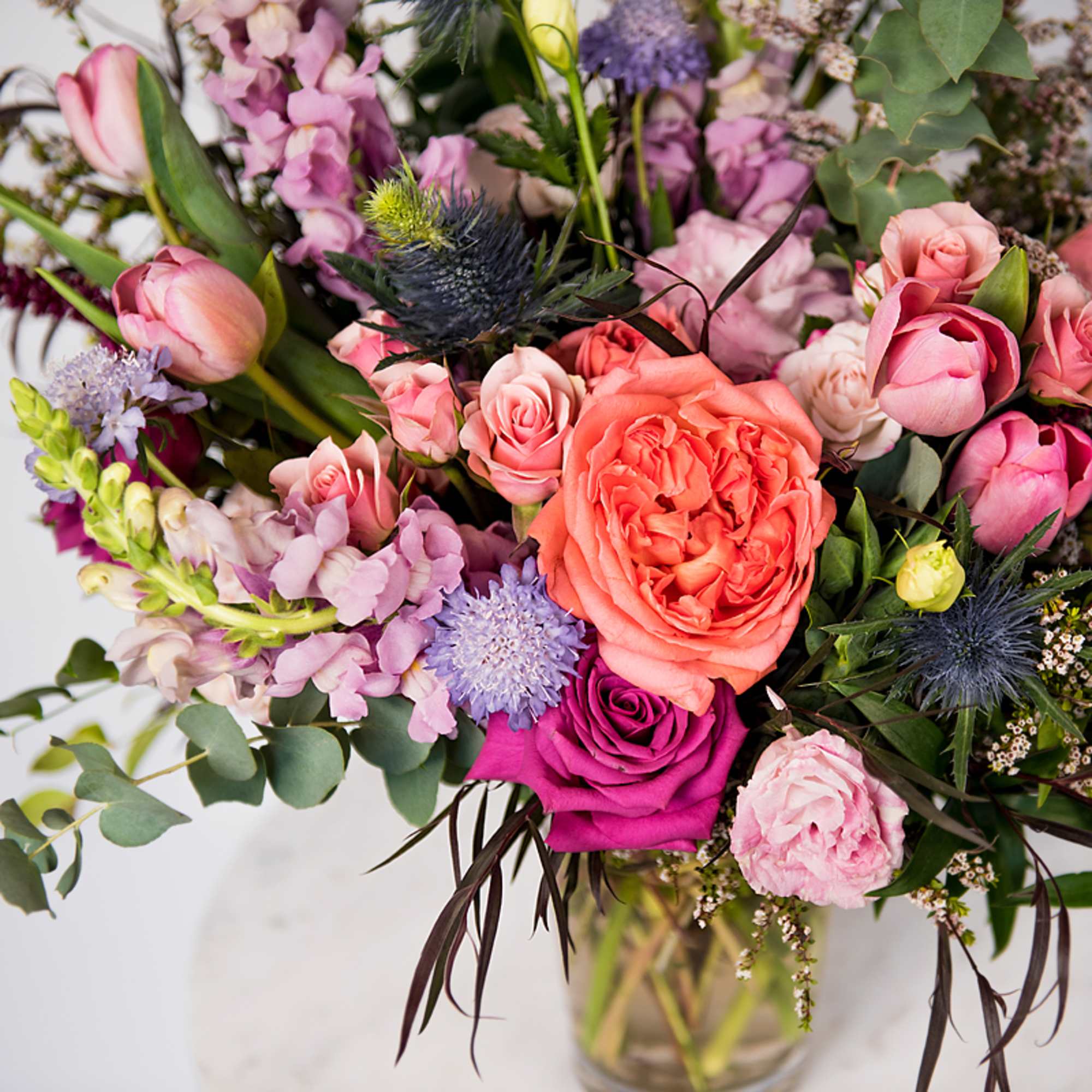 Colorful bouquet of coral, pink, and purple flowers in a clear glass vase.