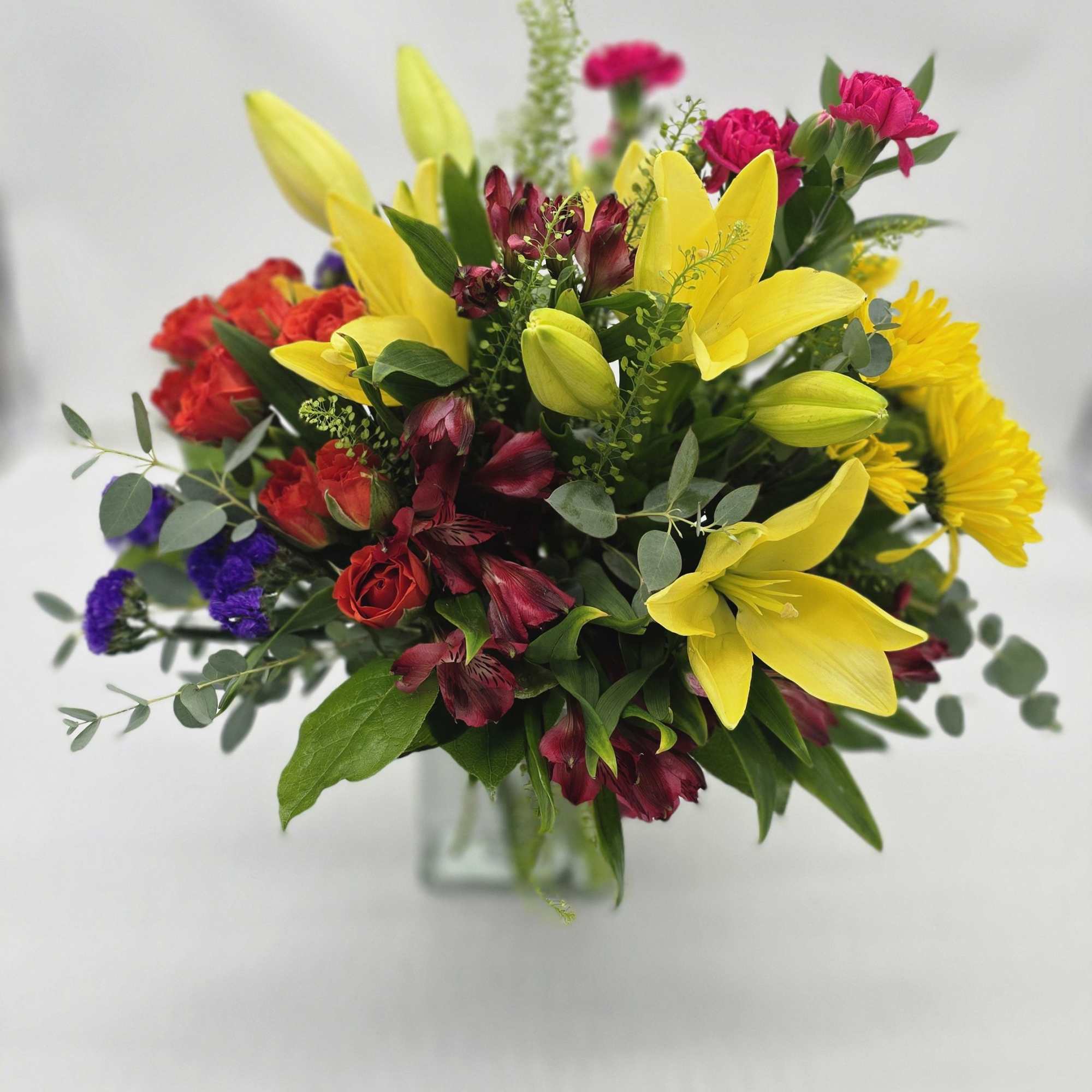 Mixed bouquet with yellow lilies, red roses, and pink carnations in a glass vase