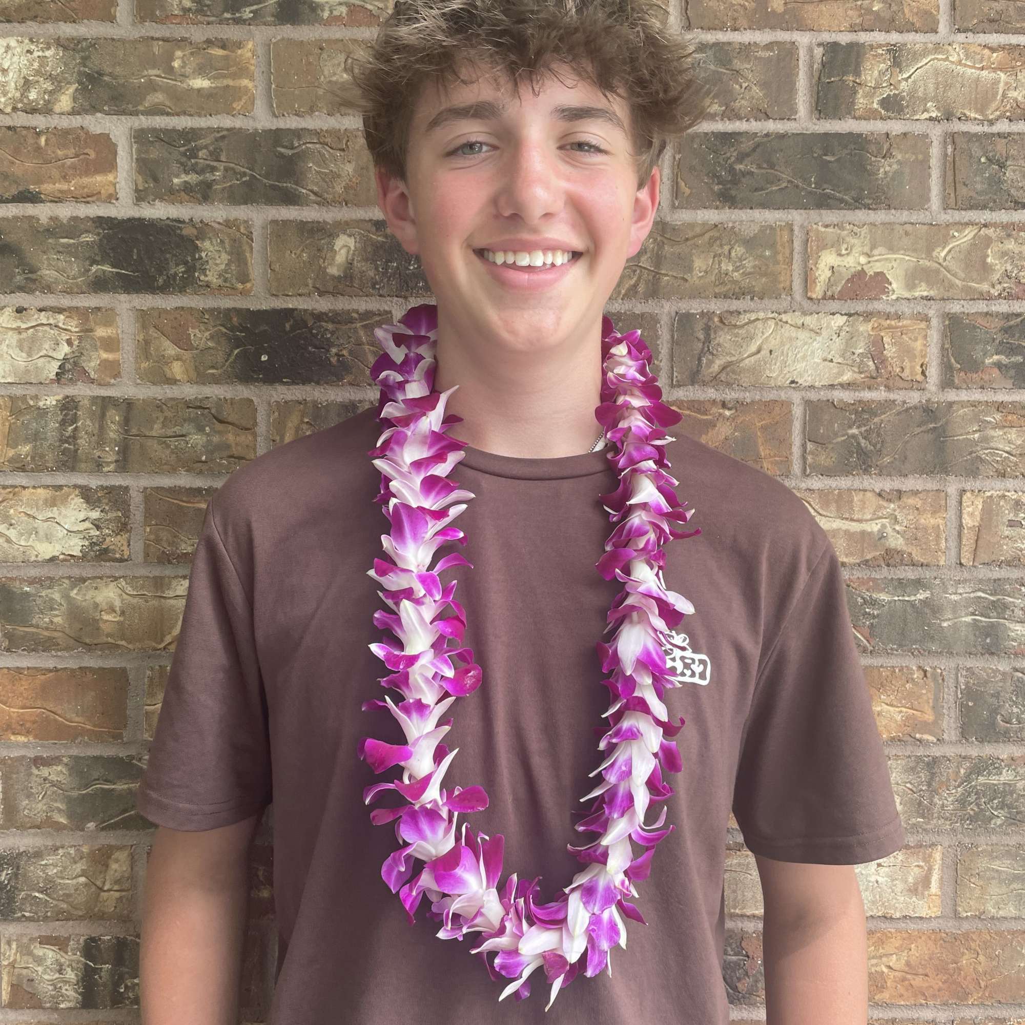 Teen wearing a purple-and-white flower lei against a brick wall