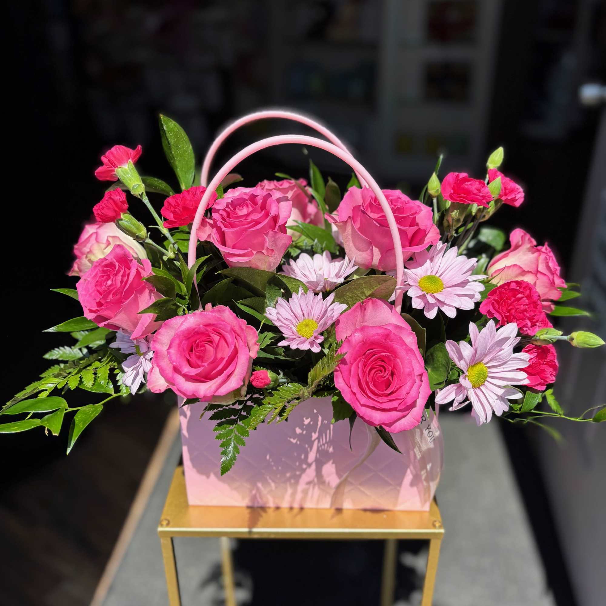 Pink roses and daisies arranged in a pink handled gift box