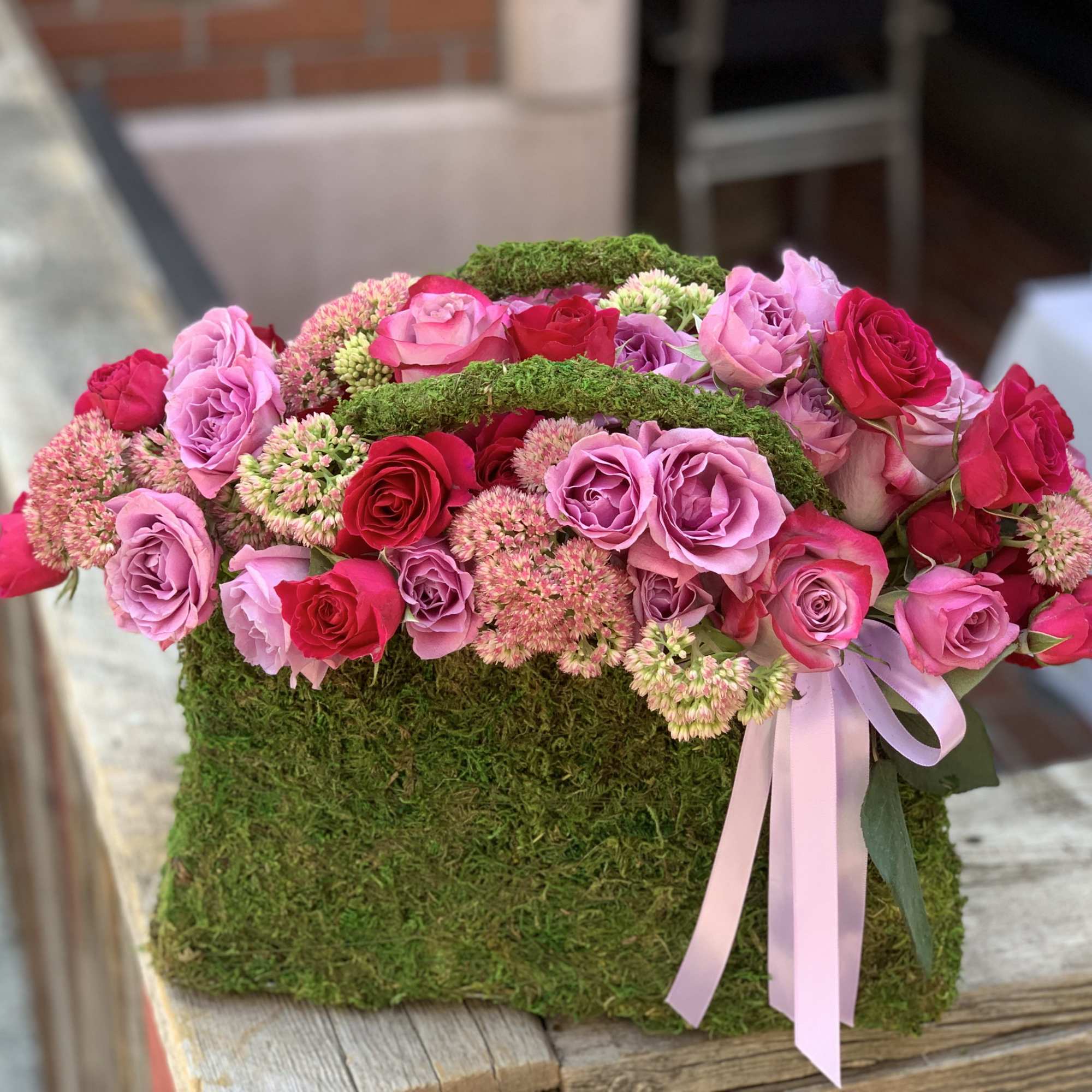 Pink and red roses arranged in a moss-covered box with a ribbon