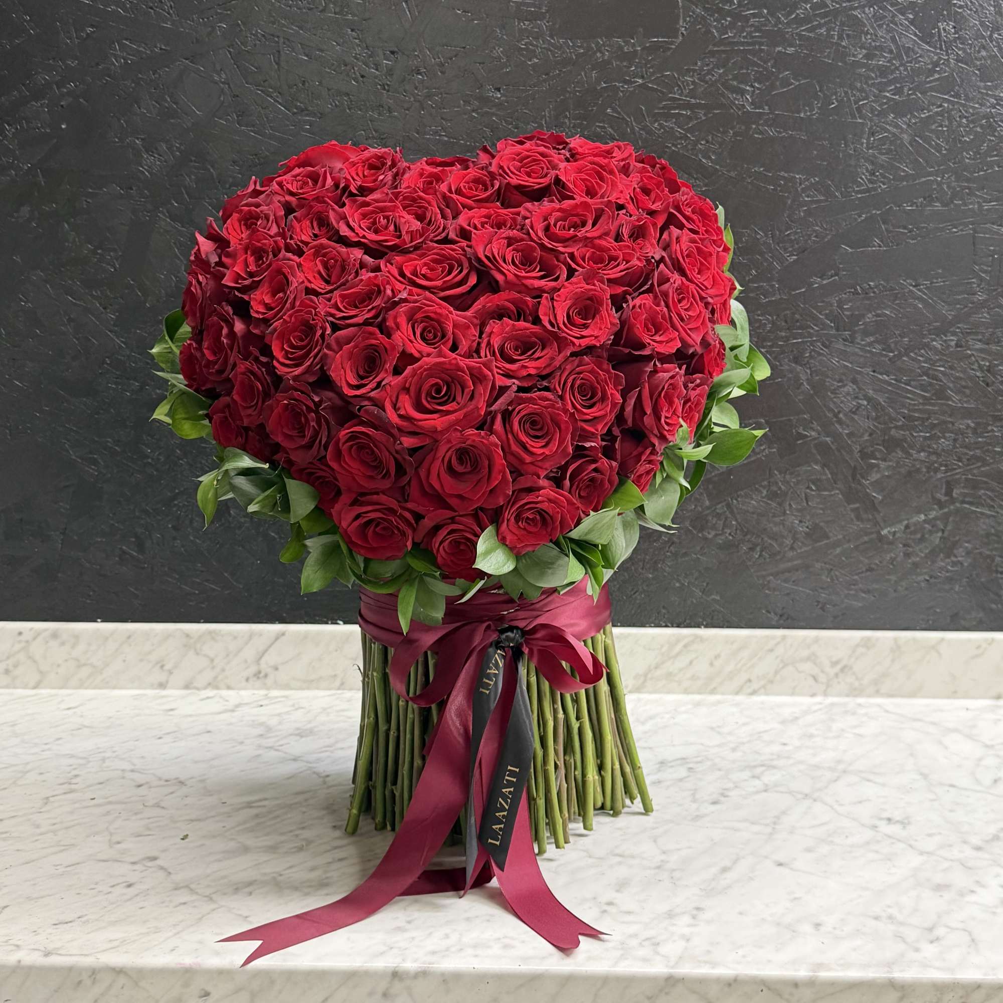Heart-shaped bouquet of red roses with a burgundy ribbon wrap