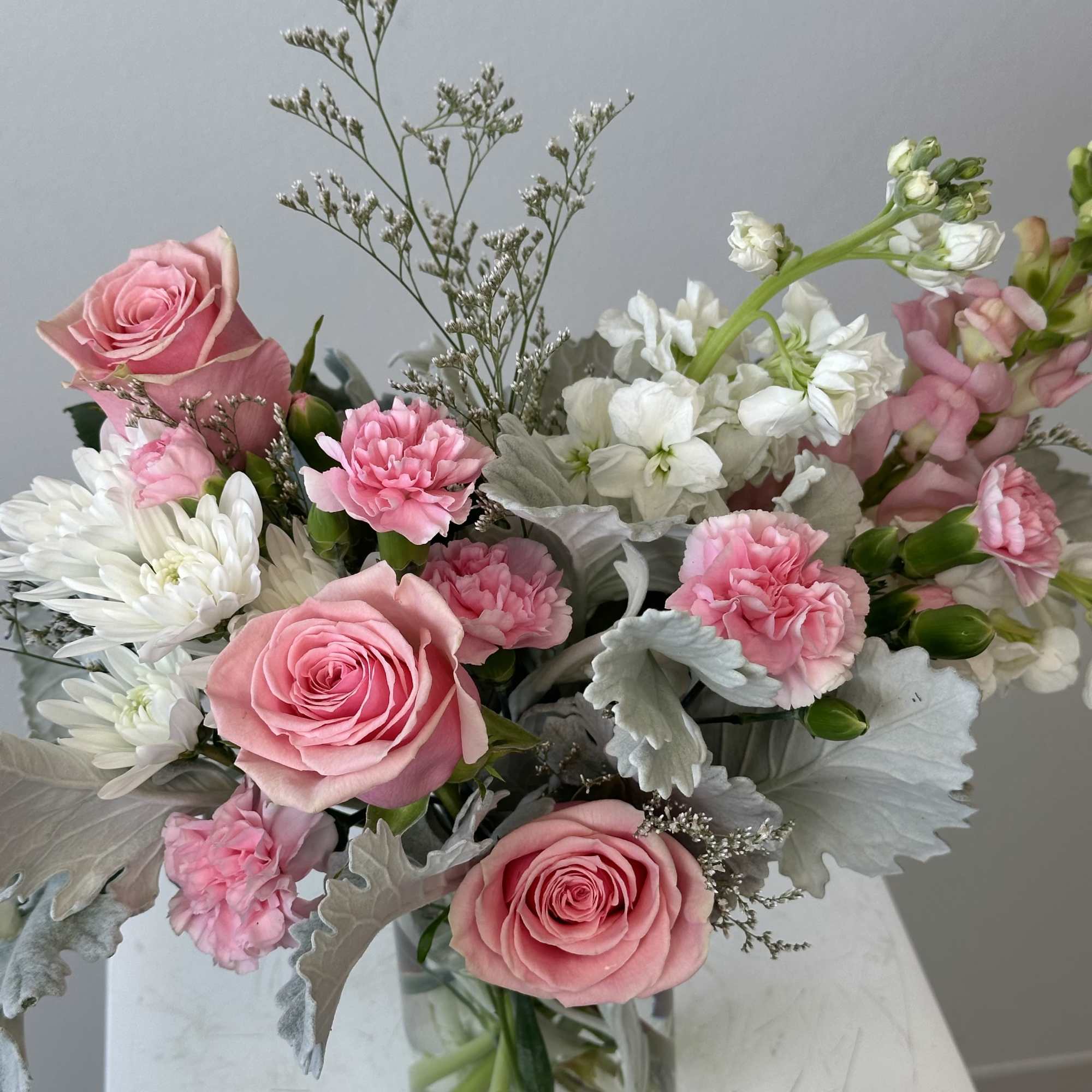 Pink roses and carnations with white mums and stock in a clear glass vase