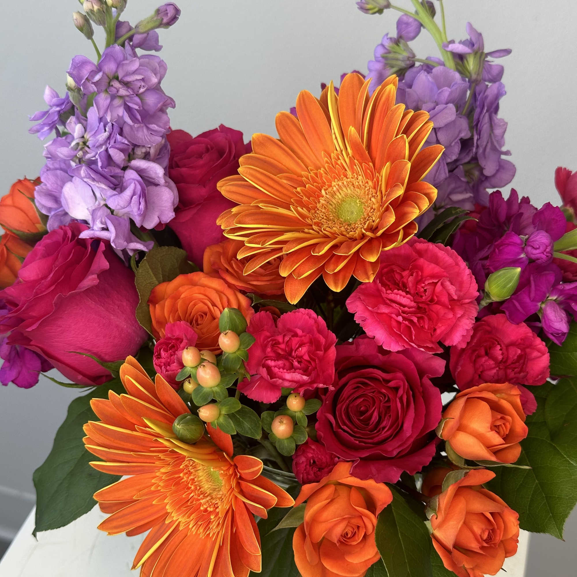 Bright mixed bouquet with orange gerberas, pink roses, and purple blooms in a glass vase