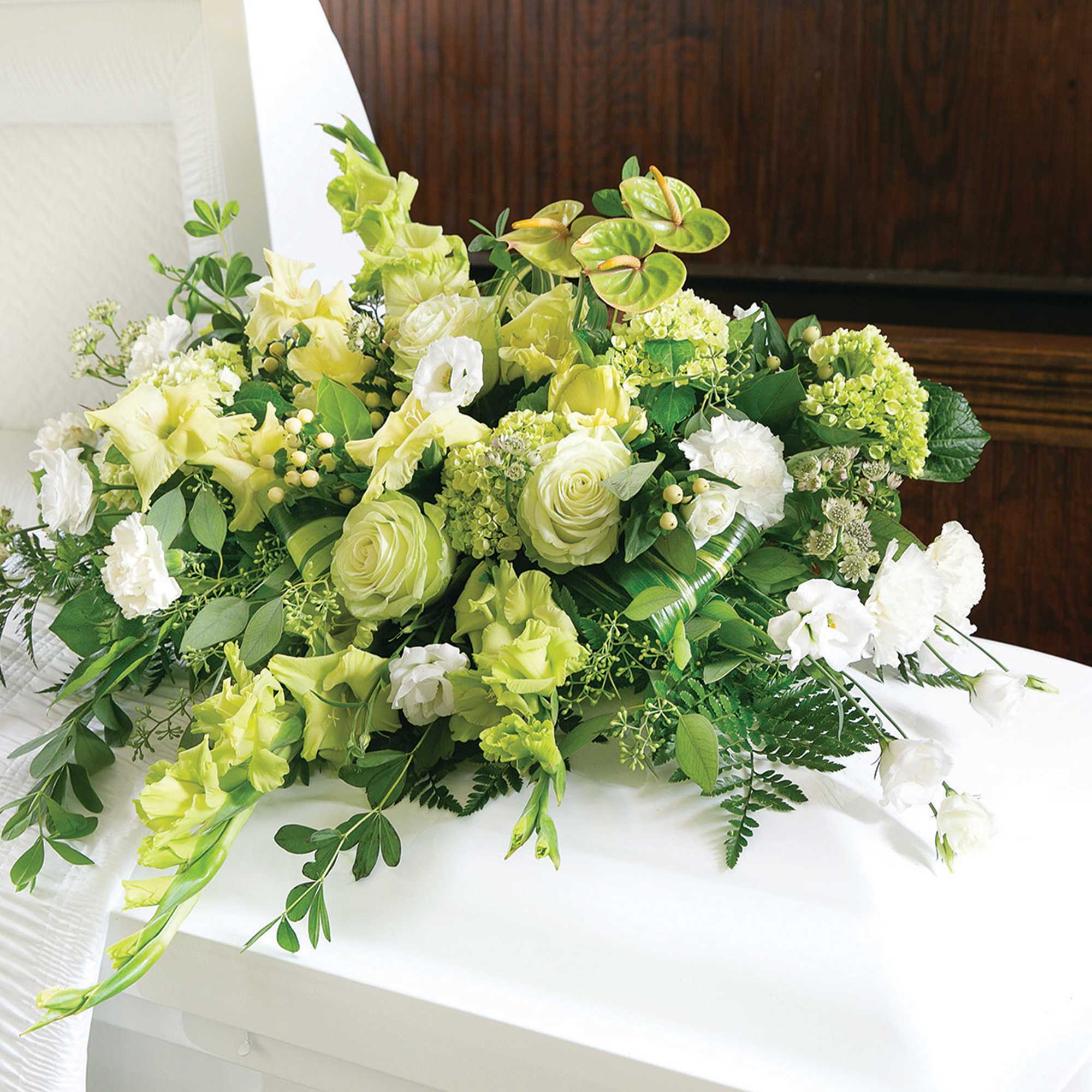 White and green casket spray with roses, carnations, and accent flowers on a white casket