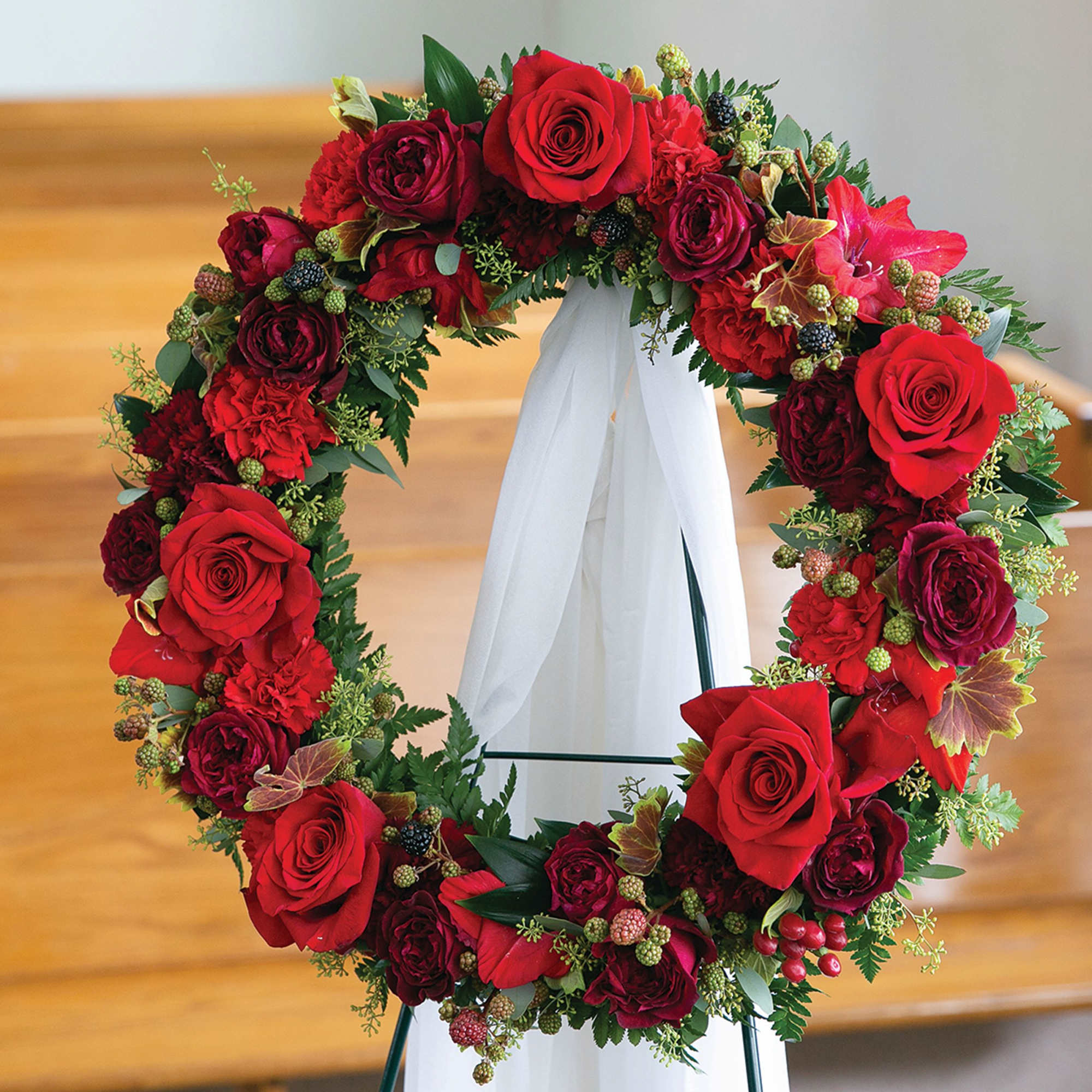 Red rose wreath on a white stand with a ribbon drape