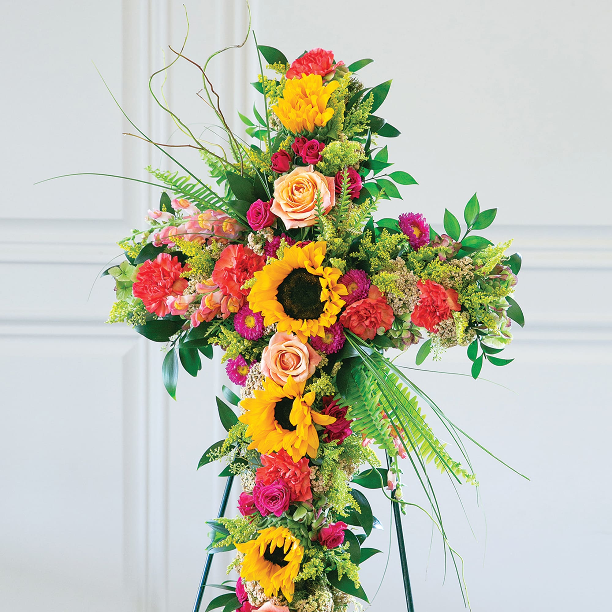 Tall floral cross on a stand with sunflowers, roses, and carnations