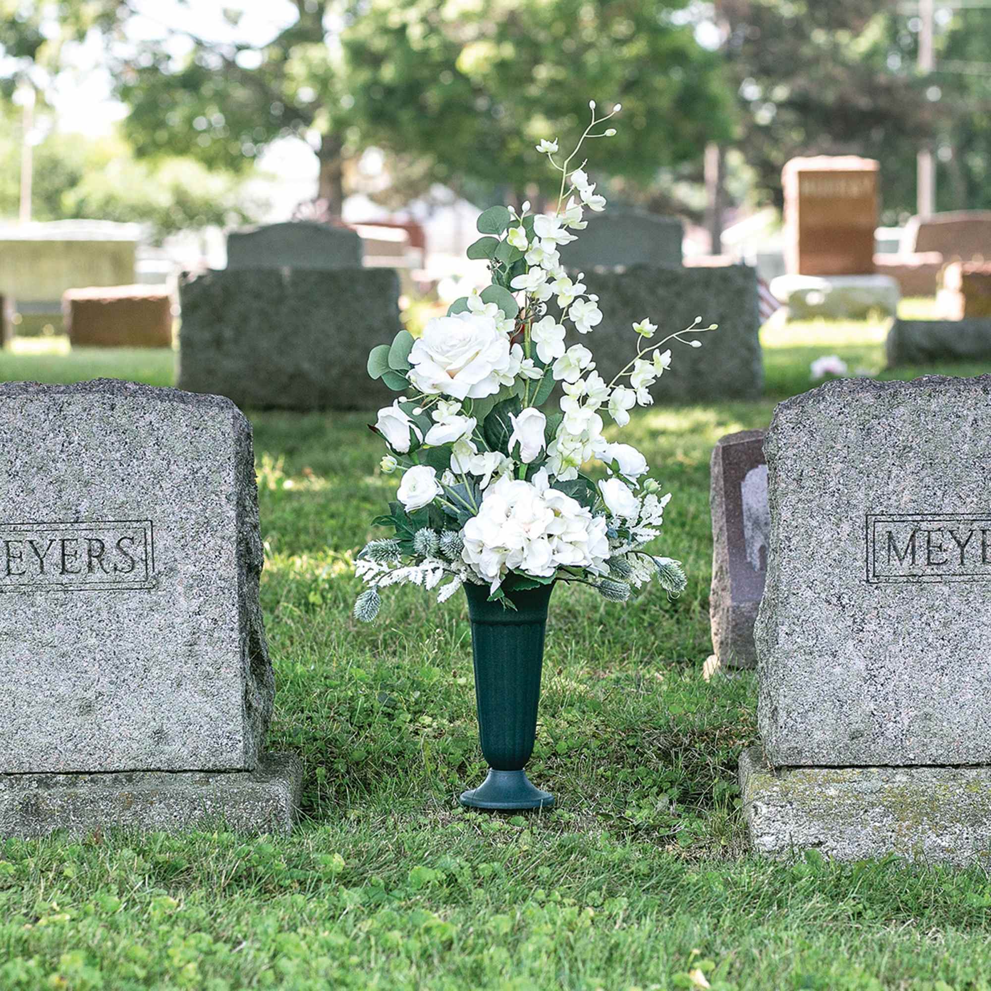 White floral arrangement in a cemetery vase between two gravestones