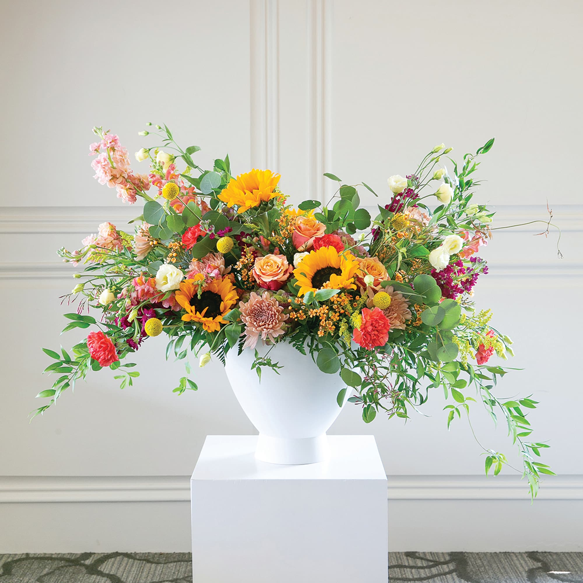 Large mixed flower arrangement in a white pedestal vase