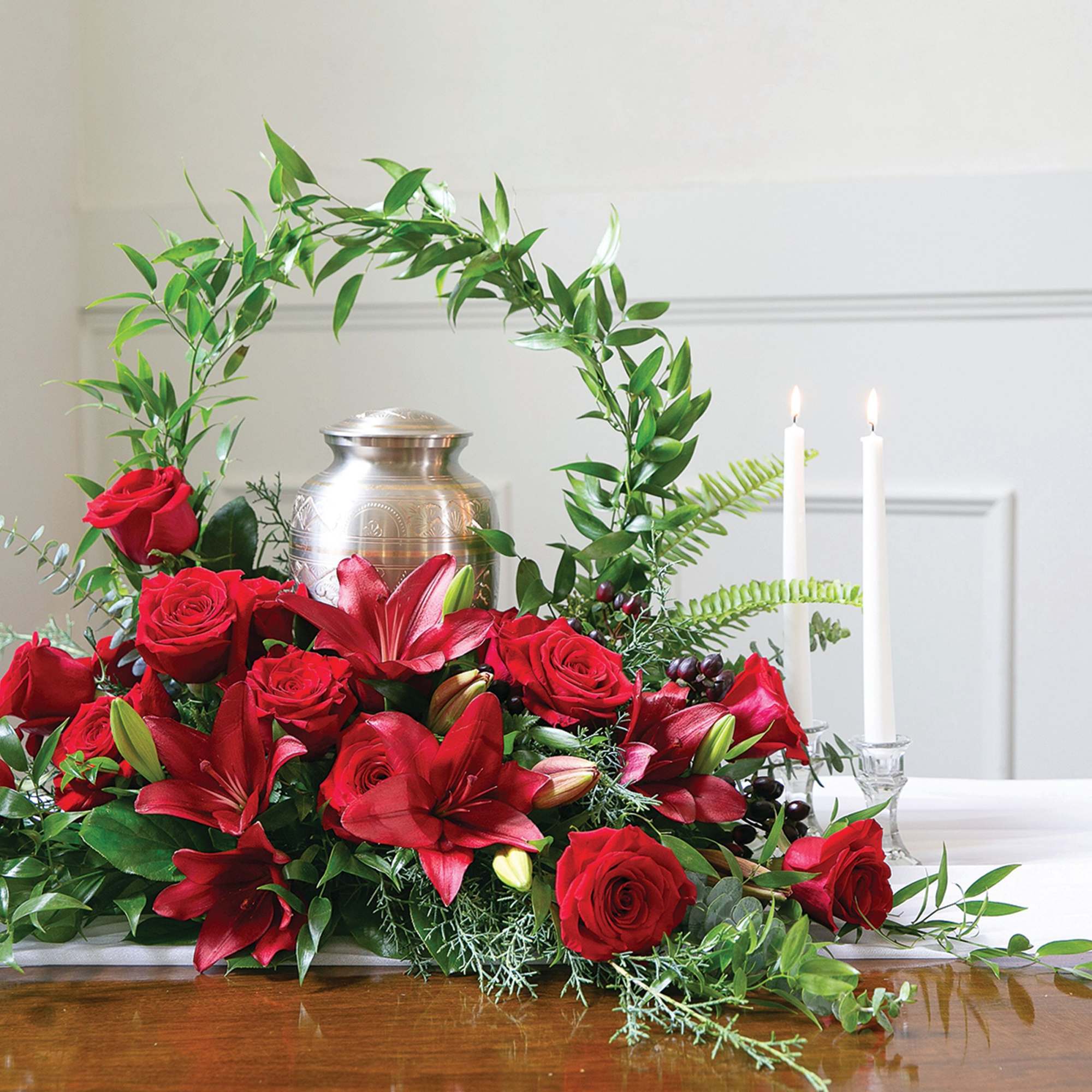 Red roses and lilies arranged around a silver urn with two white candles