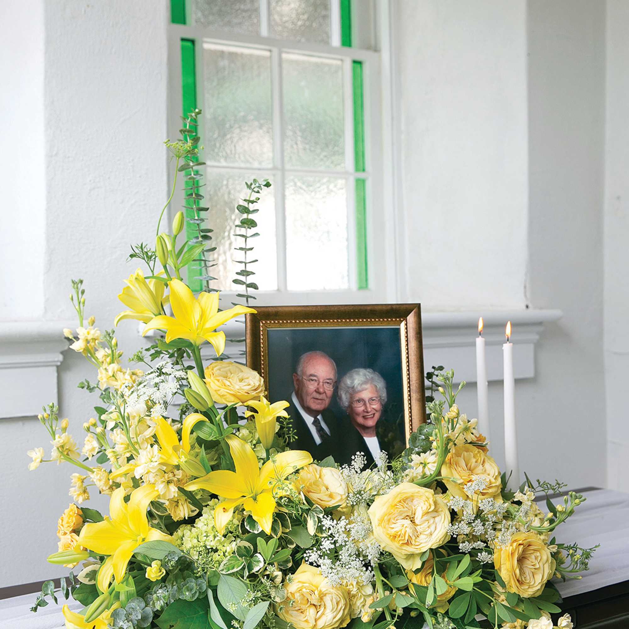 Yellow floral arrangement with a framed portrait and two lit candles