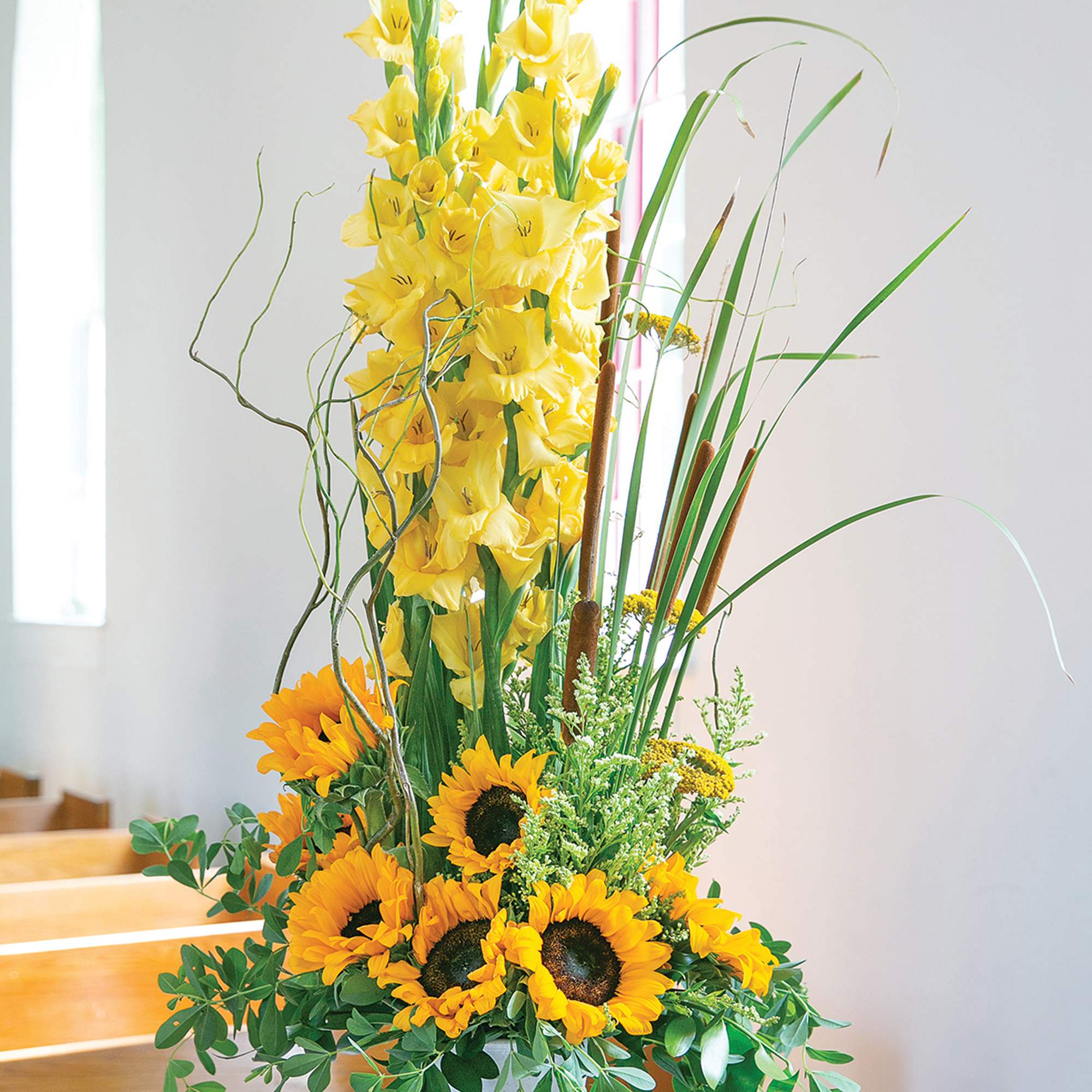 Tall floral arrangement with yellow gladiolus and sunflowers in a white vase