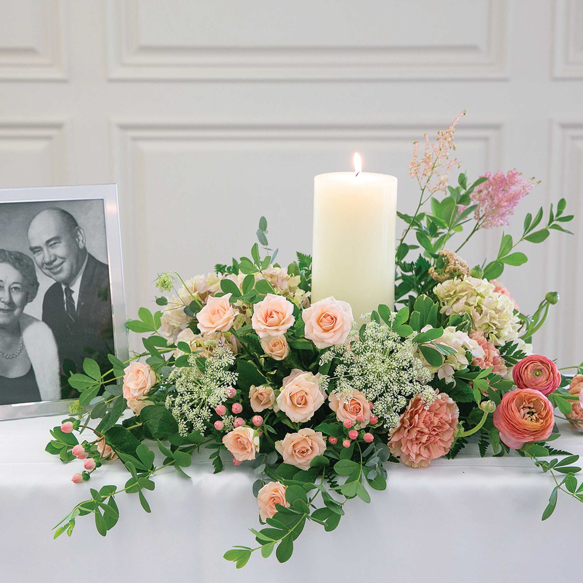 Floral memorial arrangement with a lit candle and framed black-and-white portrait