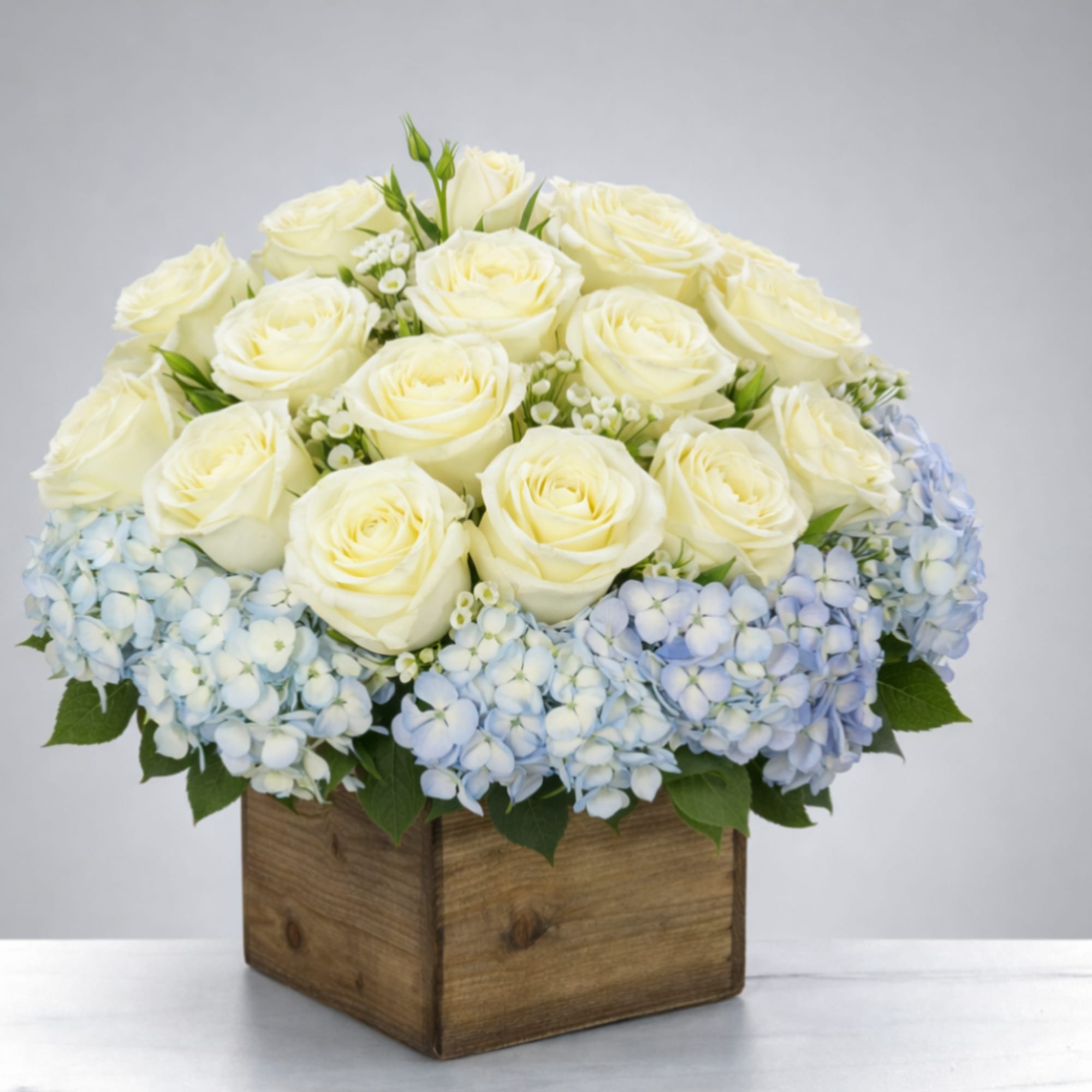 White roses and pale blue hydrangeas in a wooden box
