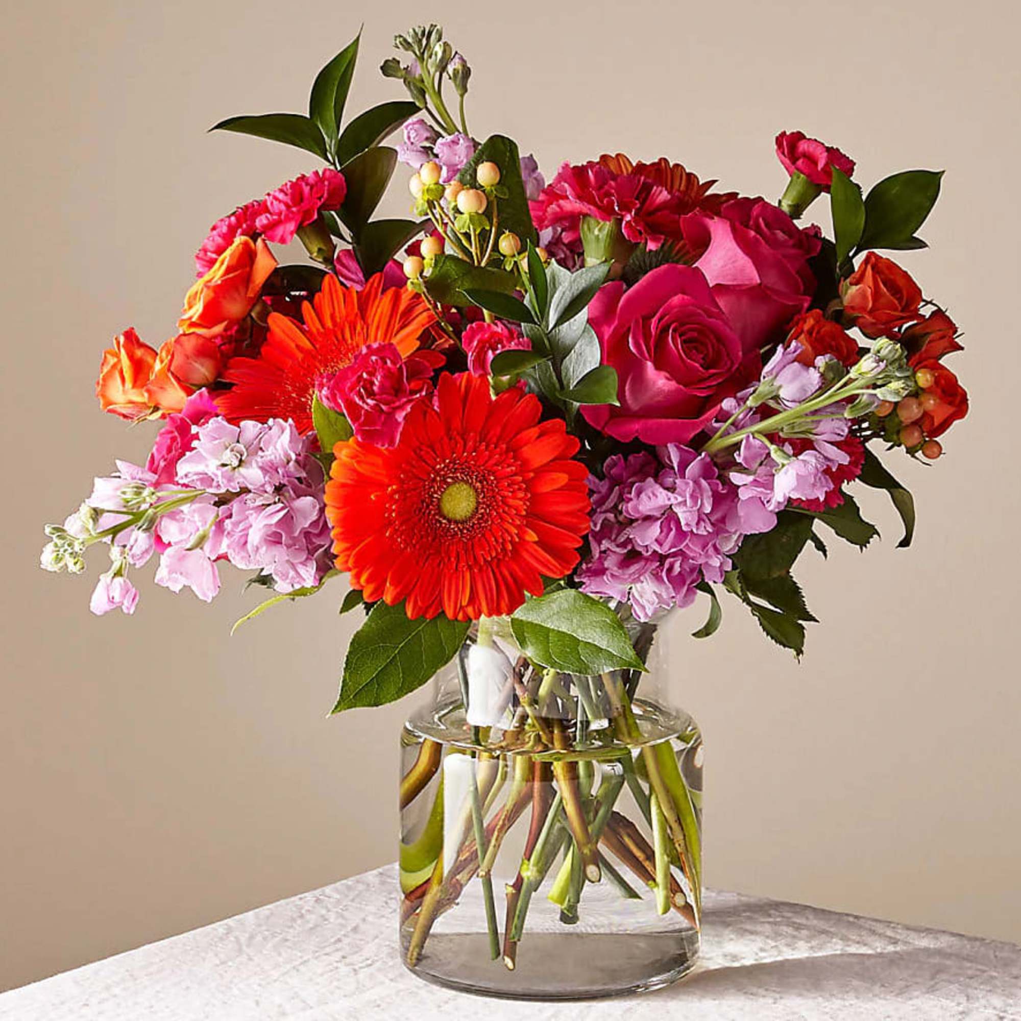 Mixed bouquet of pink, orange, and red flowers in a clear glass vase