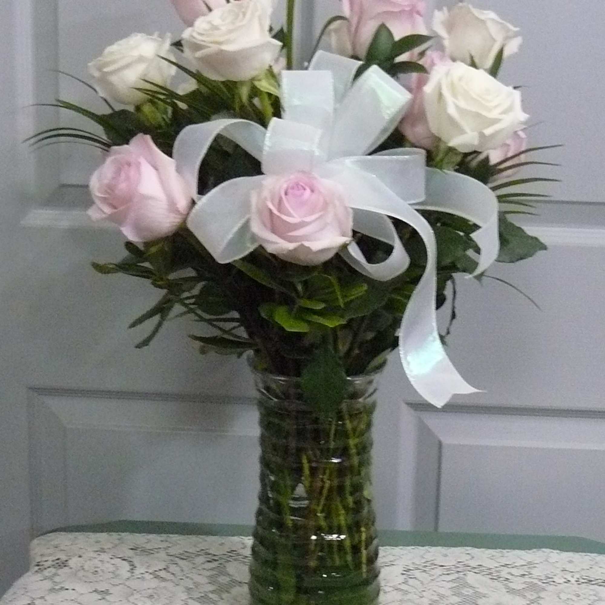Pink and white roses arranged in a glass vase with a white ribbon