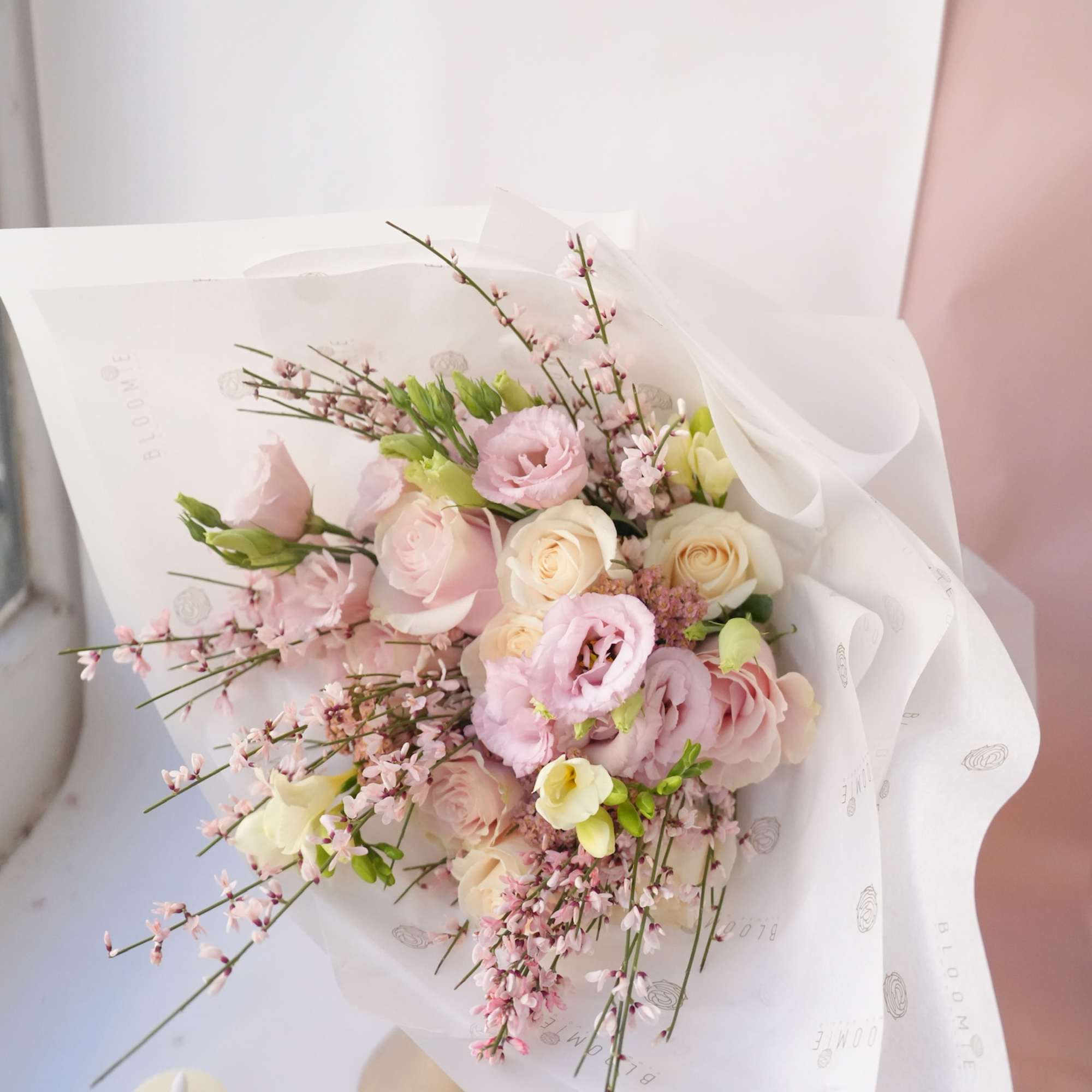 Pink and cream bouquet wrapped in white paper beside two candles