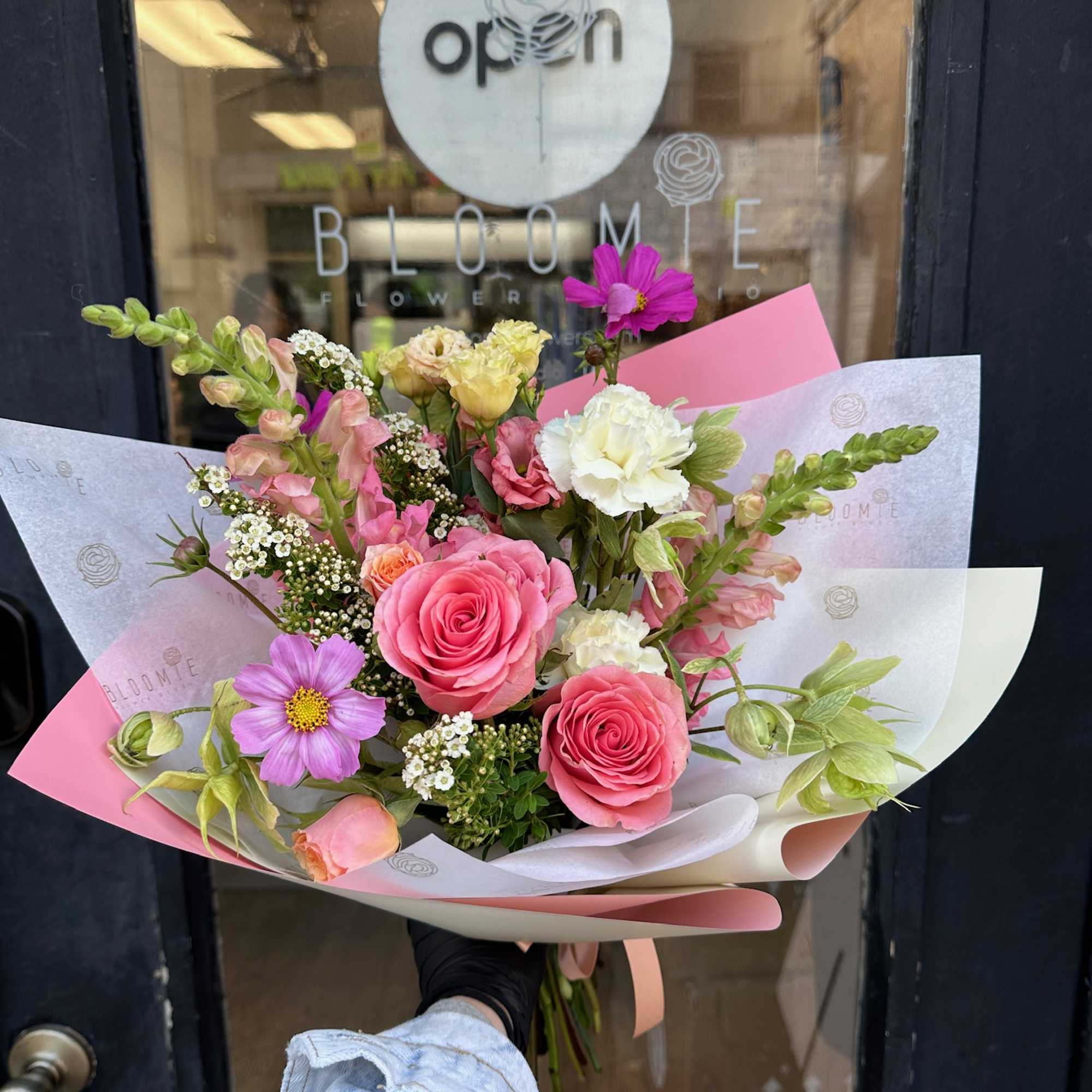 Hand-tied bouquet of pink roses and mixed blooms wrapped in pastel paper
