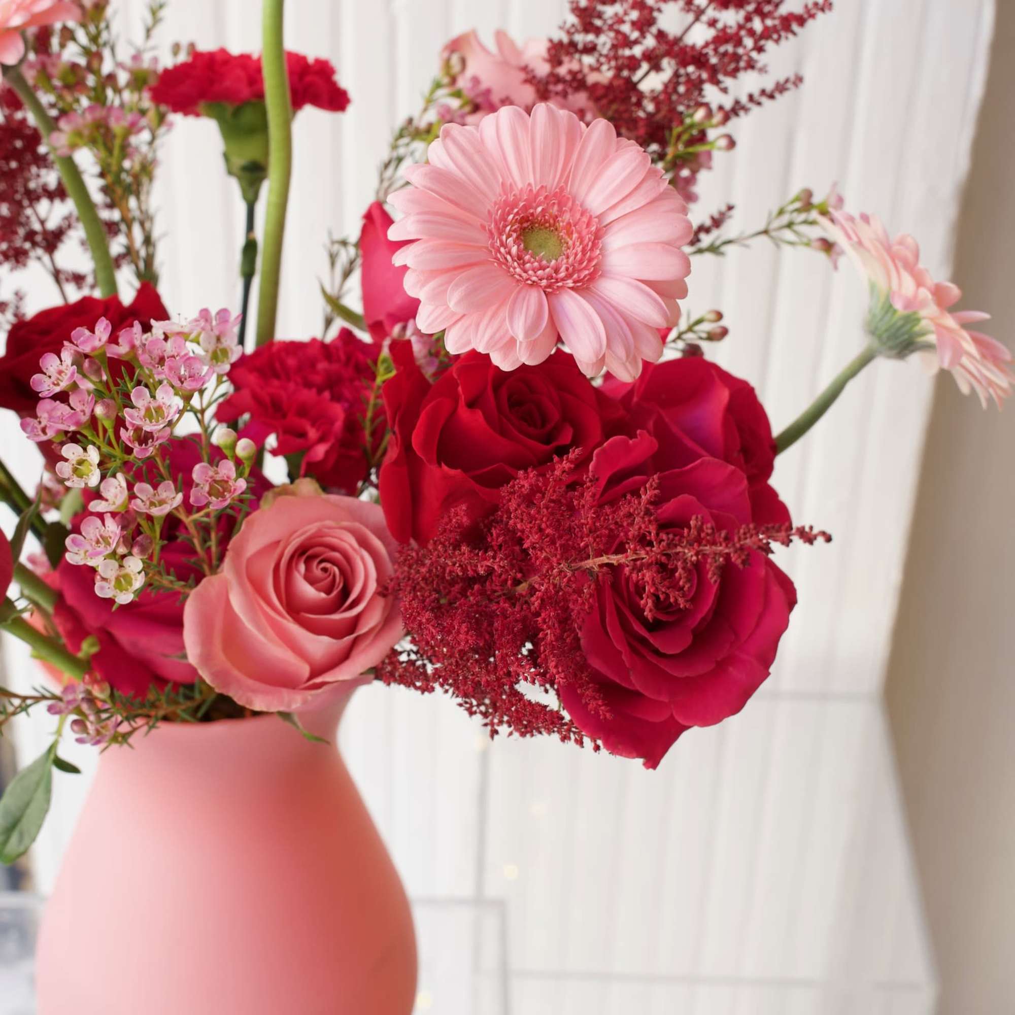 Pink and red flower arrangement in a matte pink vase