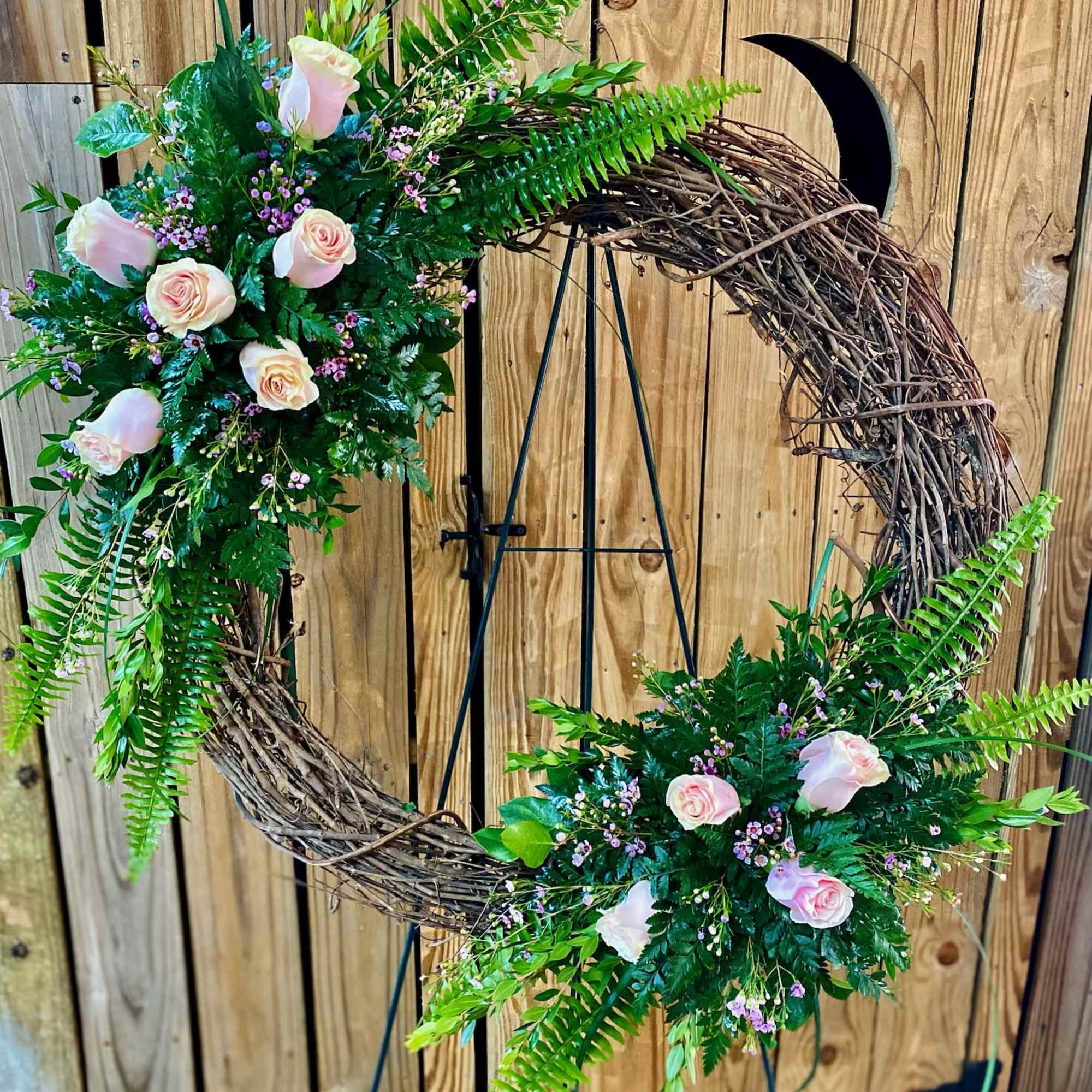 Floral crescent wreath with pale pink roses and greenery on a stand