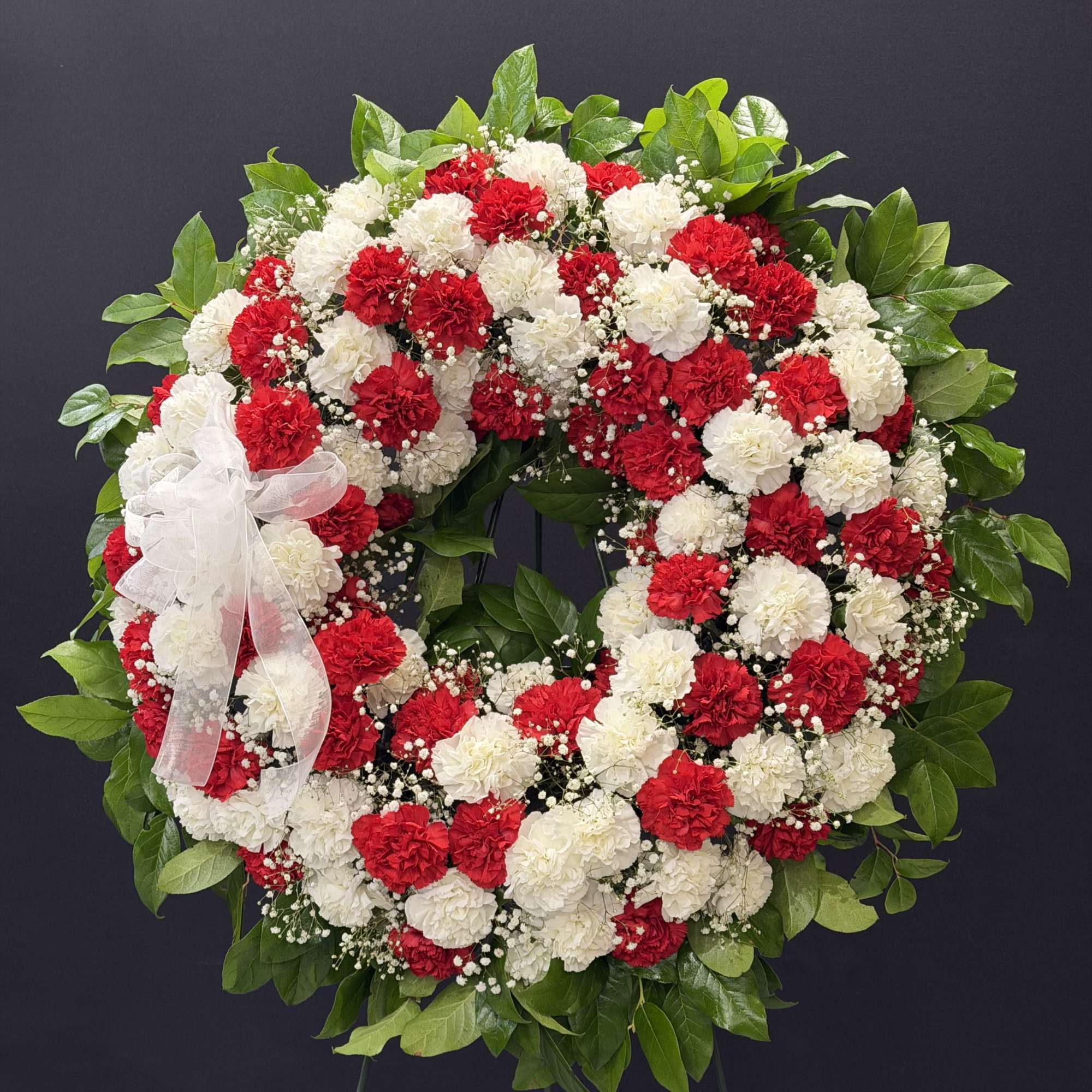 A large circular sympathy wreath crafted from red and white carnations creates