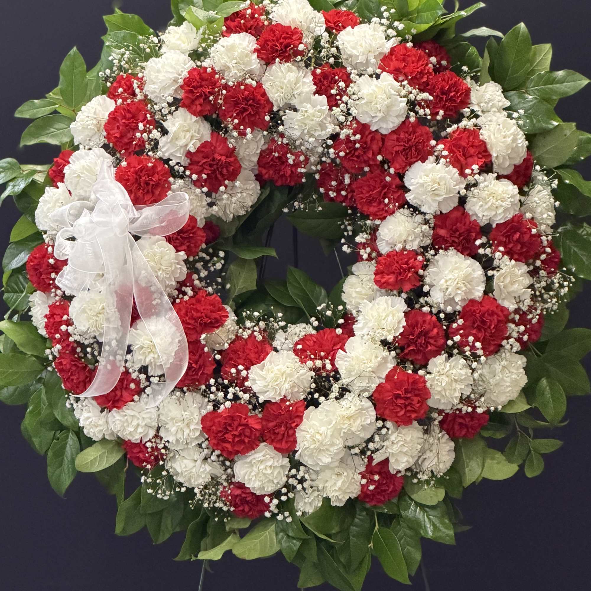 A large circular sympathy wreath crafted from red and white carnations creates