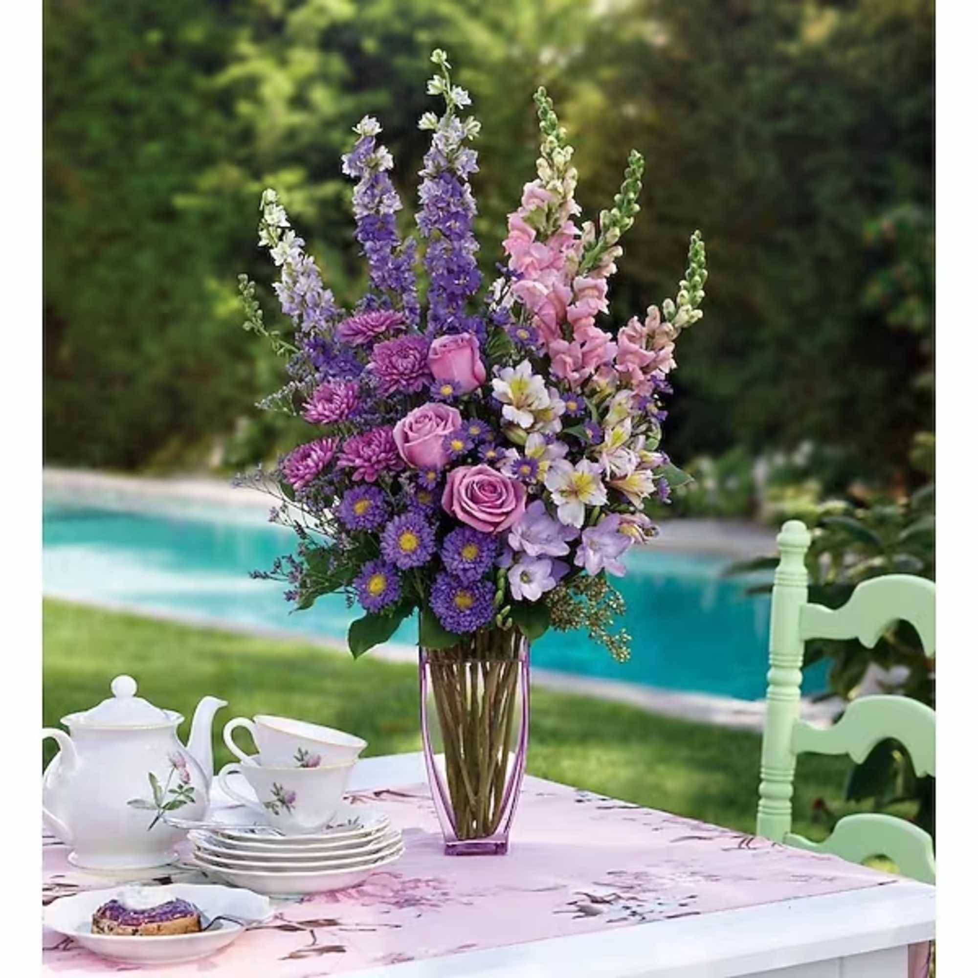 Tall purple and pink flower arrangement in a glass vase on a table