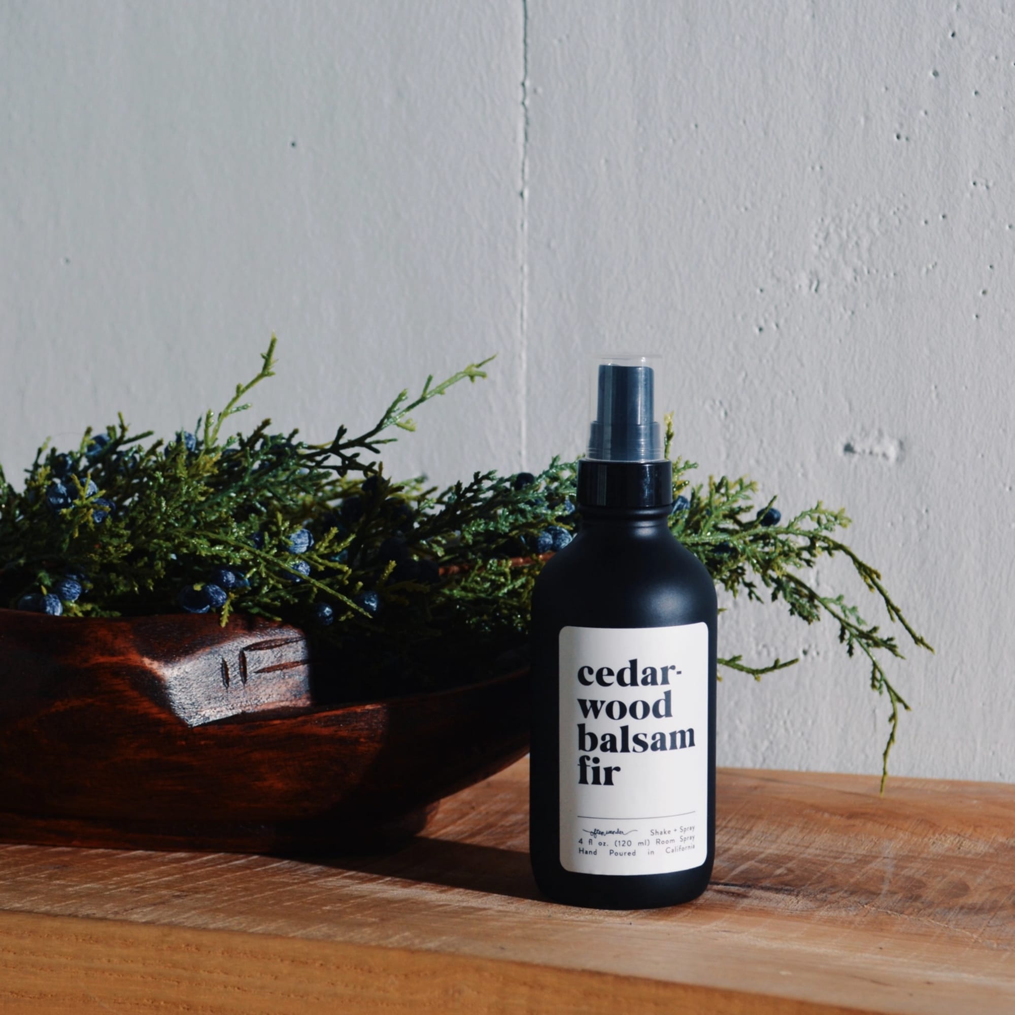 Black cedar wood balsam fir room spray bottle on wooden table beside bowl of evergreen branches